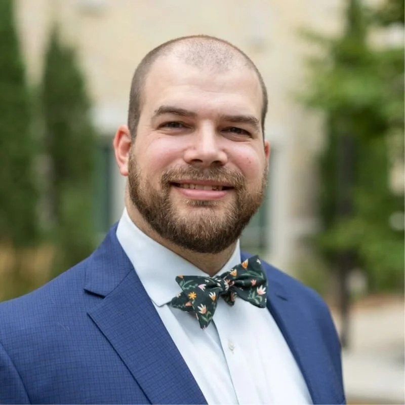 Seth Quam in a blue suit with a floral bow tie smiling outside