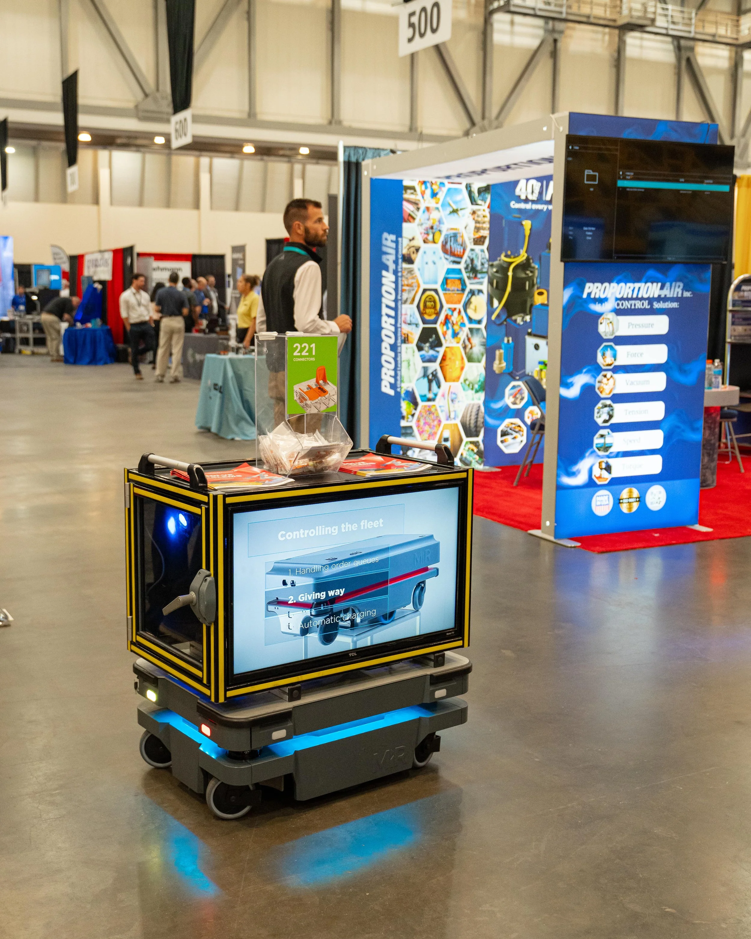 Autonomous robot with a screen displaying fleet control options, at a trade show booth for PROPORTION AIR with colorful displays and a man looking at the booth.