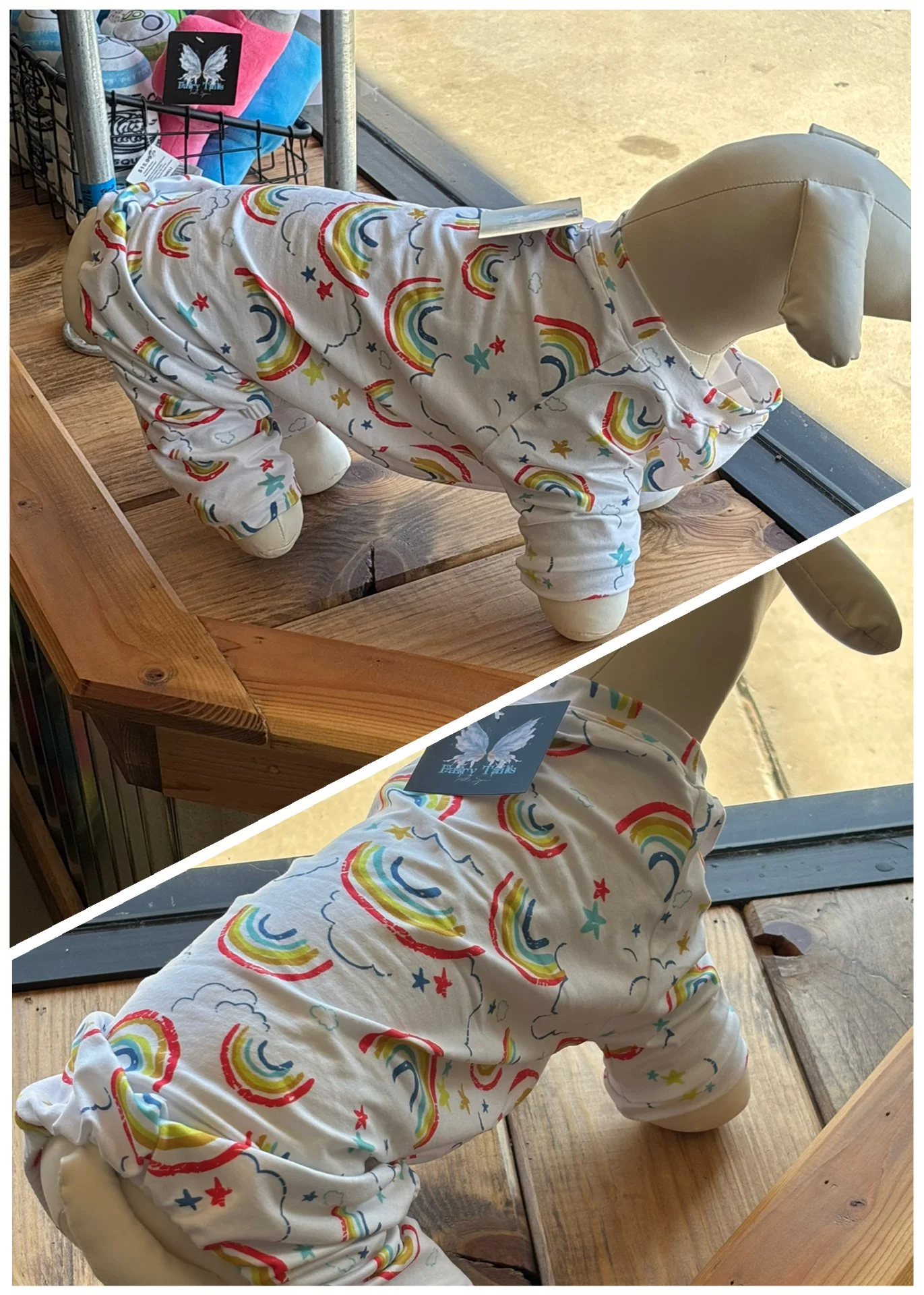 A plush dog mannequin dressed in a rainbows, clouds, and stars patterned hoodie is on display in a store. The mannequin has a fabric head and padded body, positioned on a wooden surface near a window.