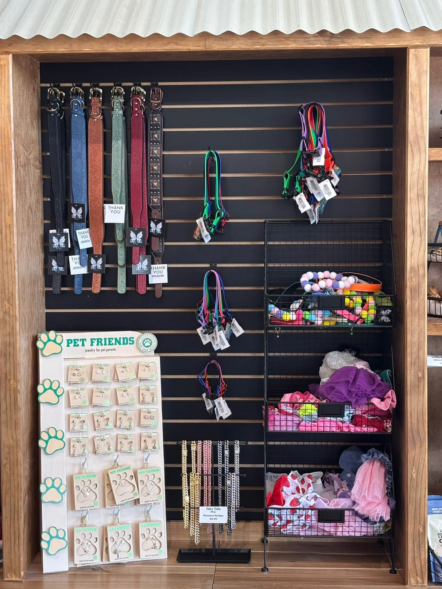 Pet accessories display with collars, leashes, toys, and jewelry for pet owners on a black slatwall with wooden frame.