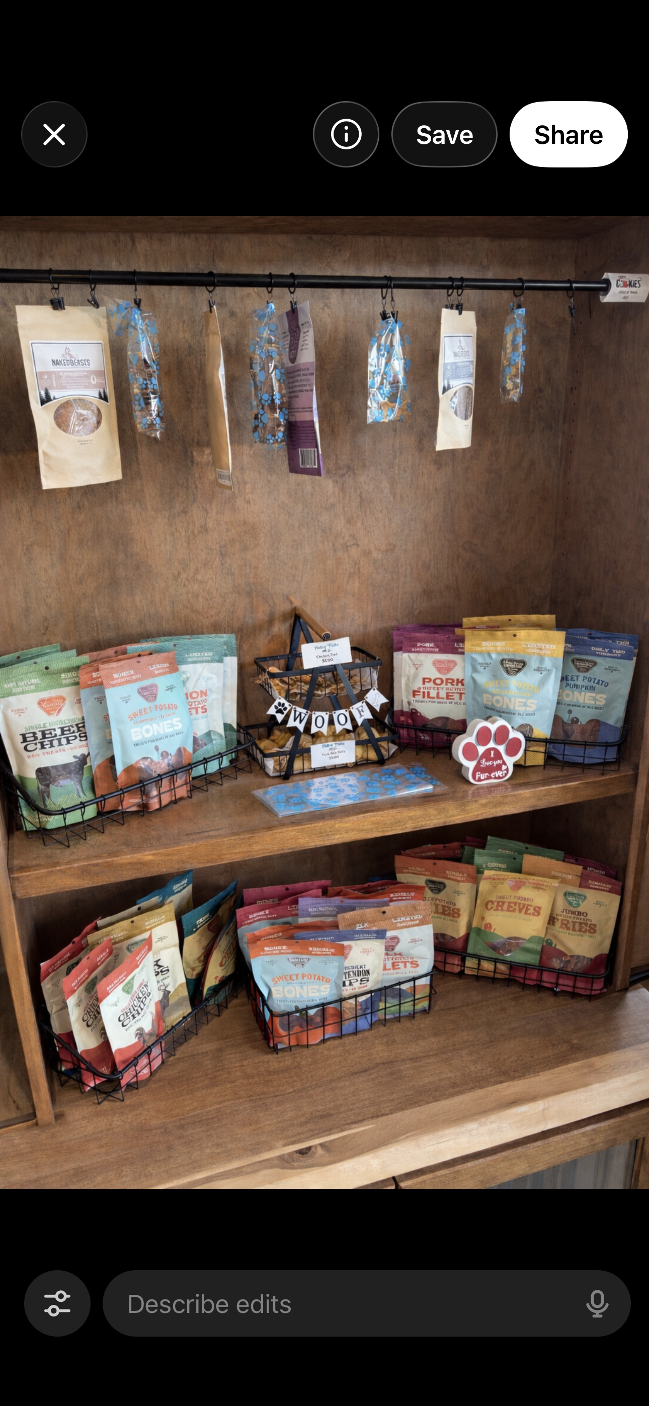 Display of various dog treats on a wooden shelf, with bags of different flavors, hanging snack packs, and decorative signs including one that says "WOOF" and another with a paw print that says "I love you Fur-ever."