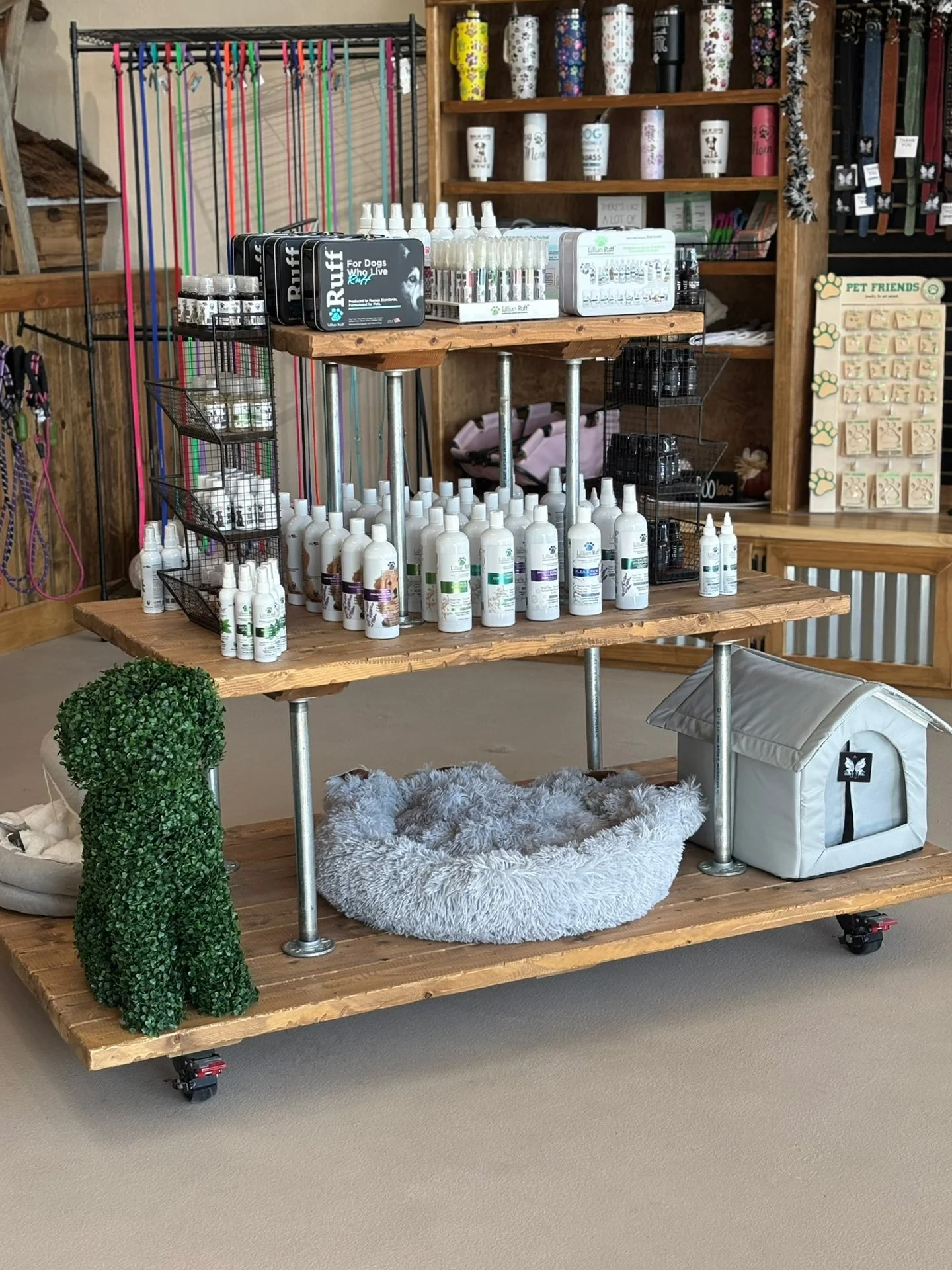 Display of pet grooming and care products on a multi-tiered wooden cart, including bottles, sprays, and pet accessories, with a background of pet-themed items on wooden shelves.
