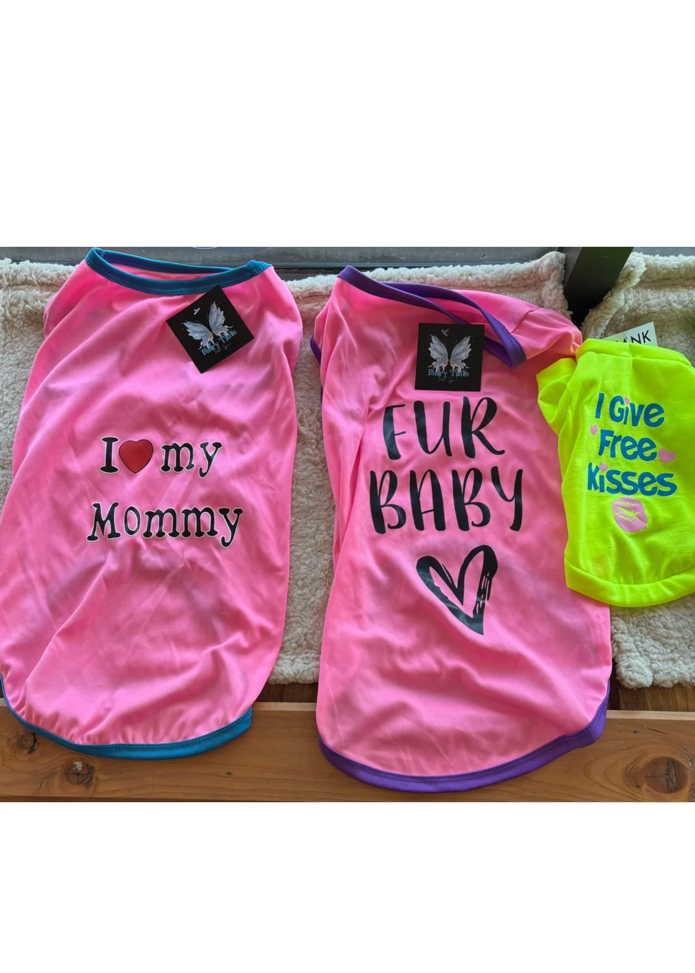 Pink dog shirts with different messages, one saying "I love my mommy" and another saying "Fur Baby" with a purple trim, plus a bright yellow item with the words "I give free kisses" and a kiss mark.