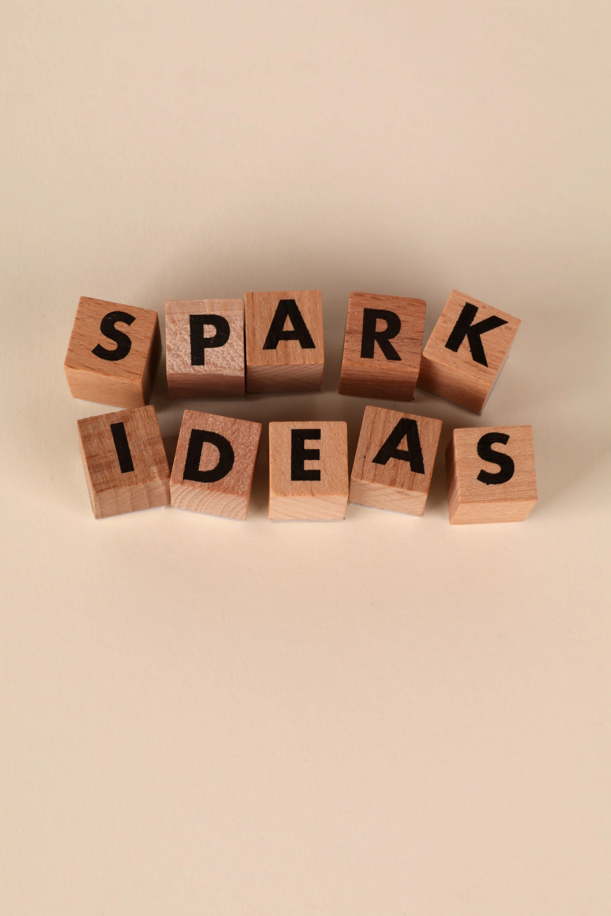 Wooden blocks with black letters spelling out "SPARK IDEAS" on a plain light background.