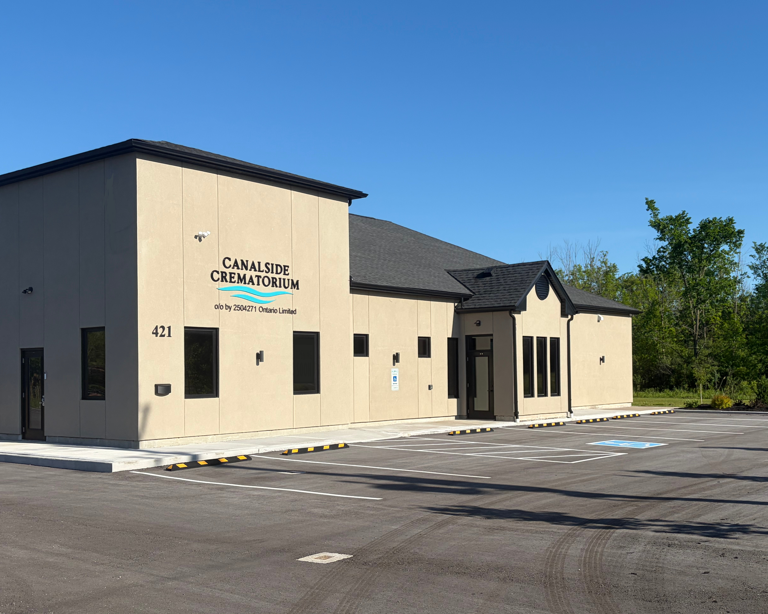 Exterior view of the Canalside Crematorium building with a parking lot in the foreground and clear blue sky overhead.