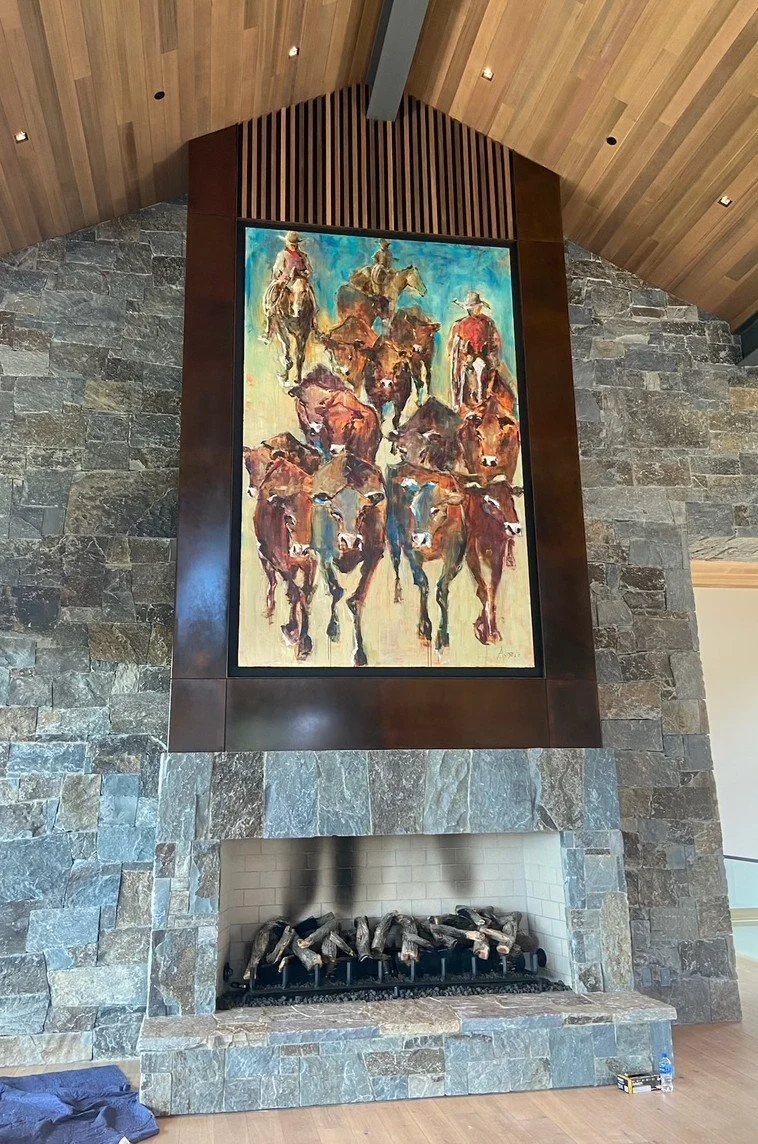 A large painting of horseback riders hanging above a stone fireplace in a room with a wood-paneled ceiling.