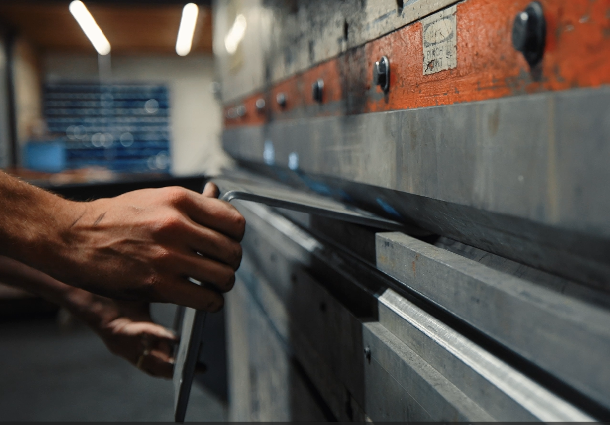 Close-up of a person's hands working with a hand tool on a long metal surface, possibly in a workshop or industrial setting.