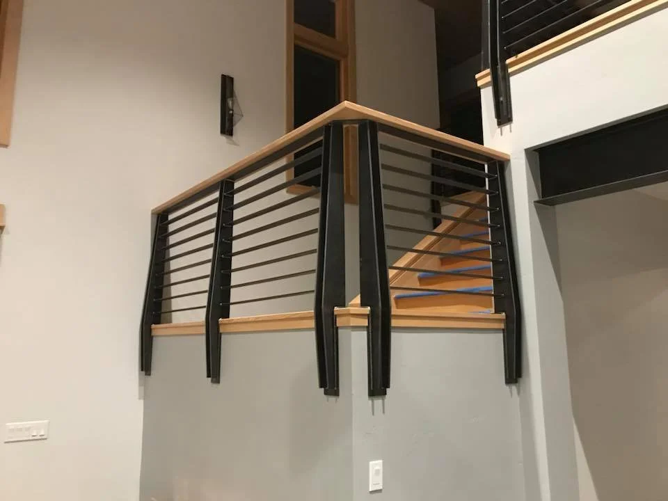 Interior view of a staircase and balcony railing with black metal and wooden handrails in a modern home.