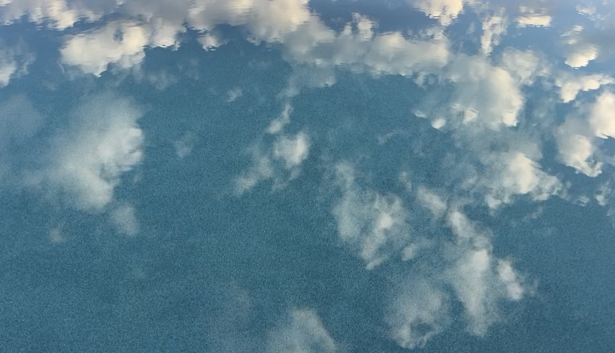 Reflection of white clouds on a bright blue water surface.