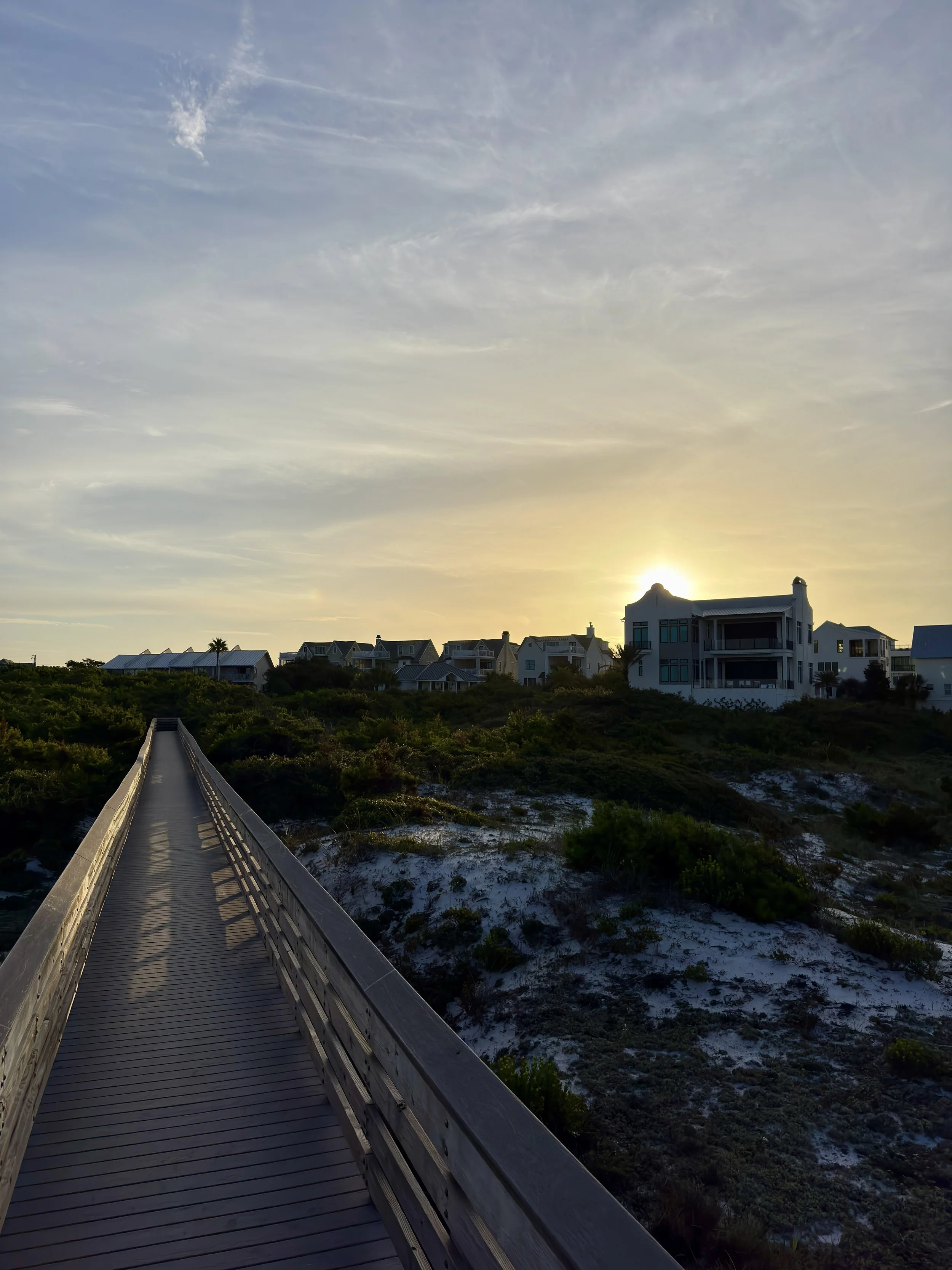 A boardwalk leading to houses on a hill at sunset with a partly cloudy sky.