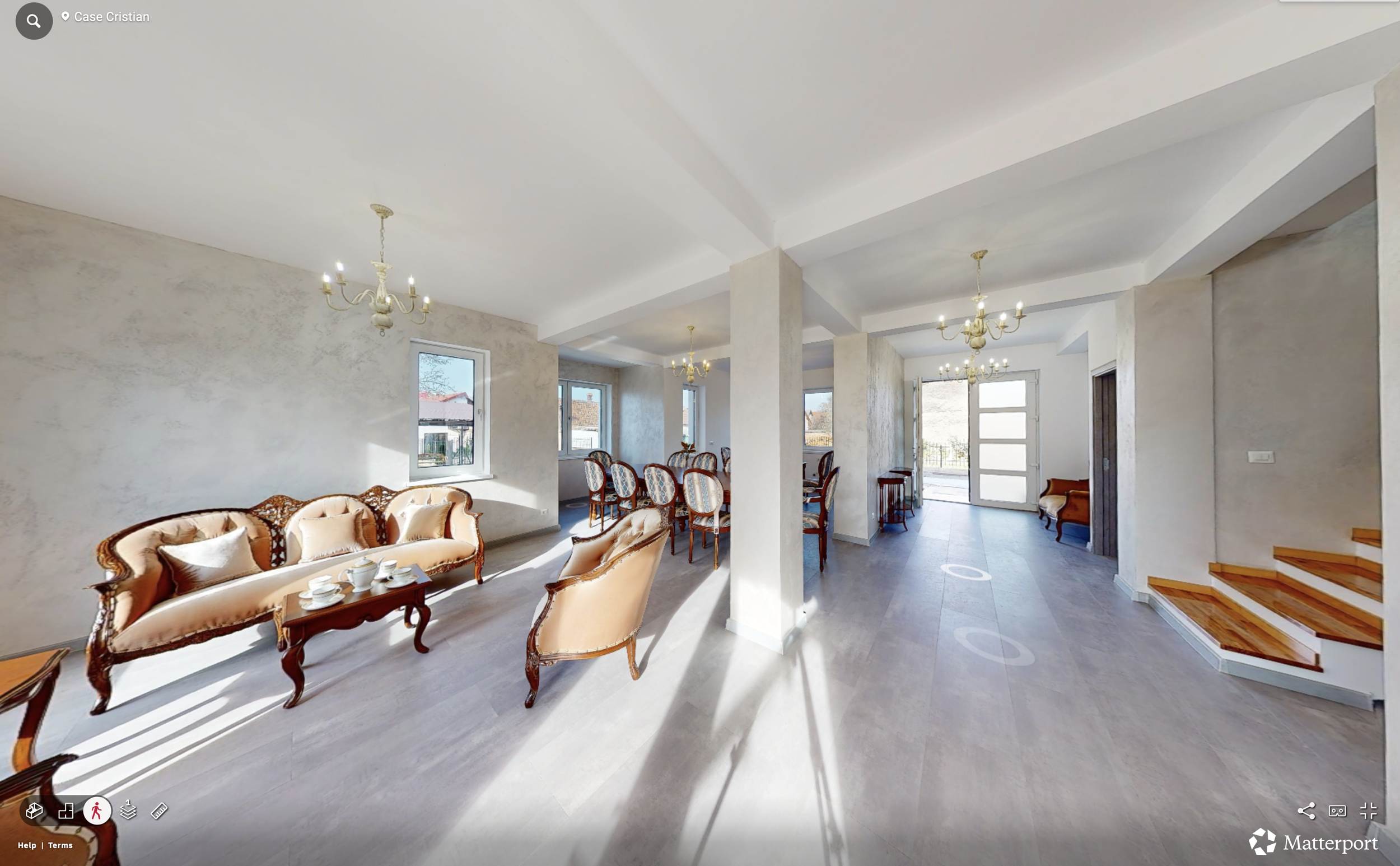 Living room with antique style furniture, chandelier lighting, large windows, and staircase with wooden steps.