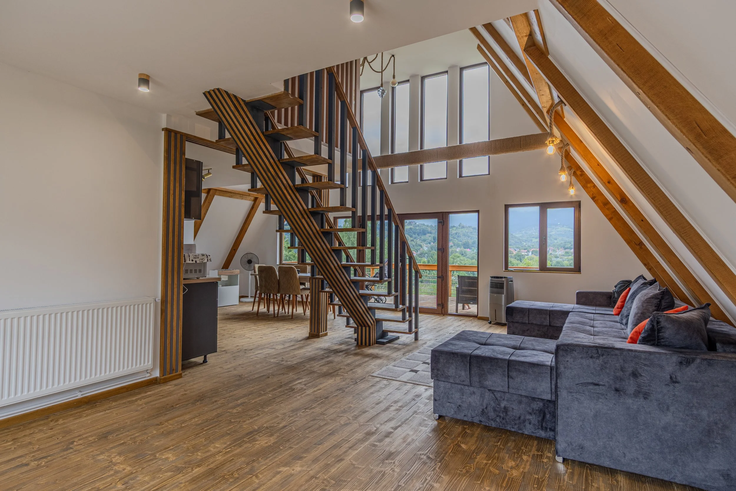 Open living space with a modern staircase, large windows, gray sectional sofa, and wooden floors.