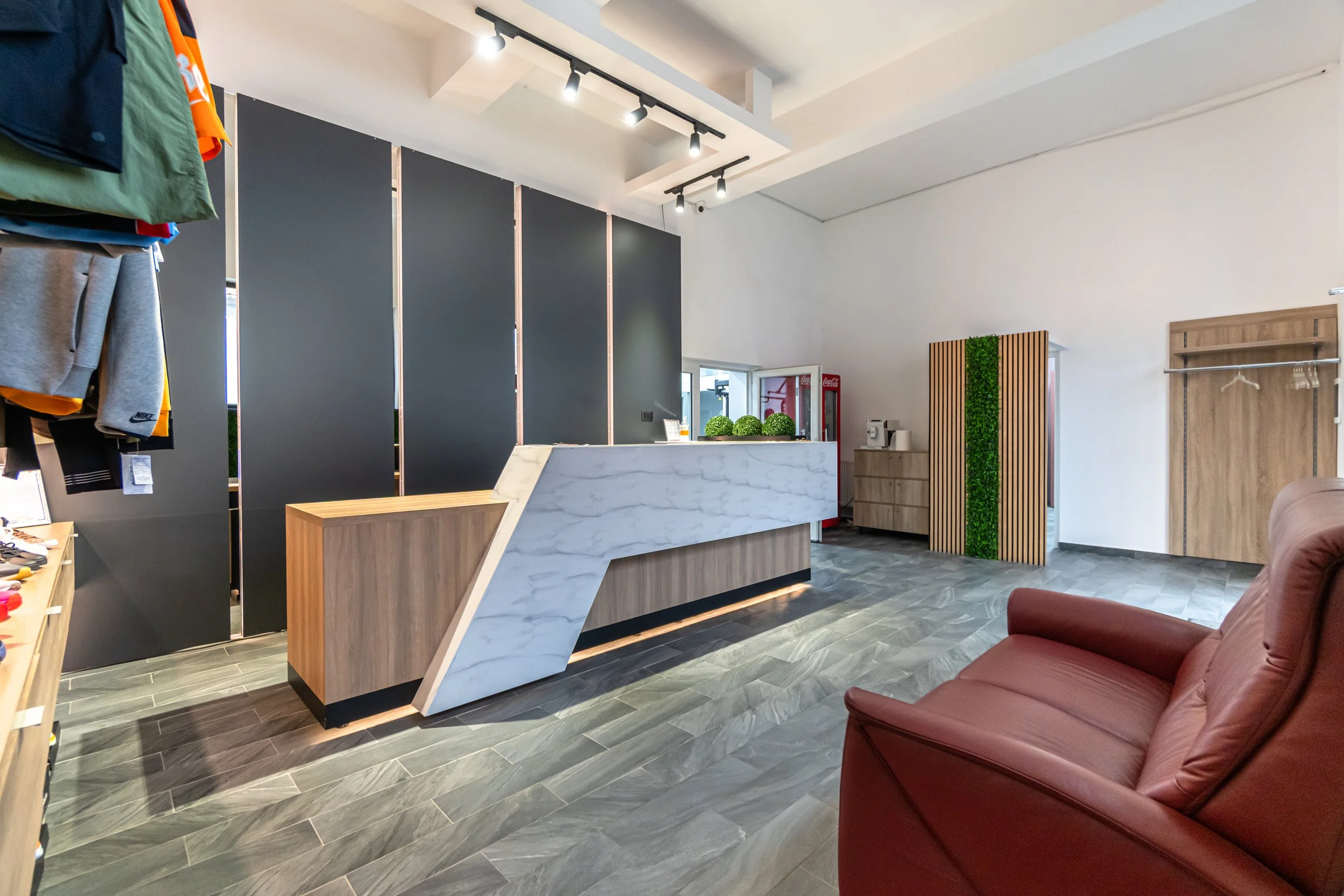 Modern retail store interior with a checkout counter, a red couch in the foreground, a clothing display on the left, and a vending machine and decor on the back wall.