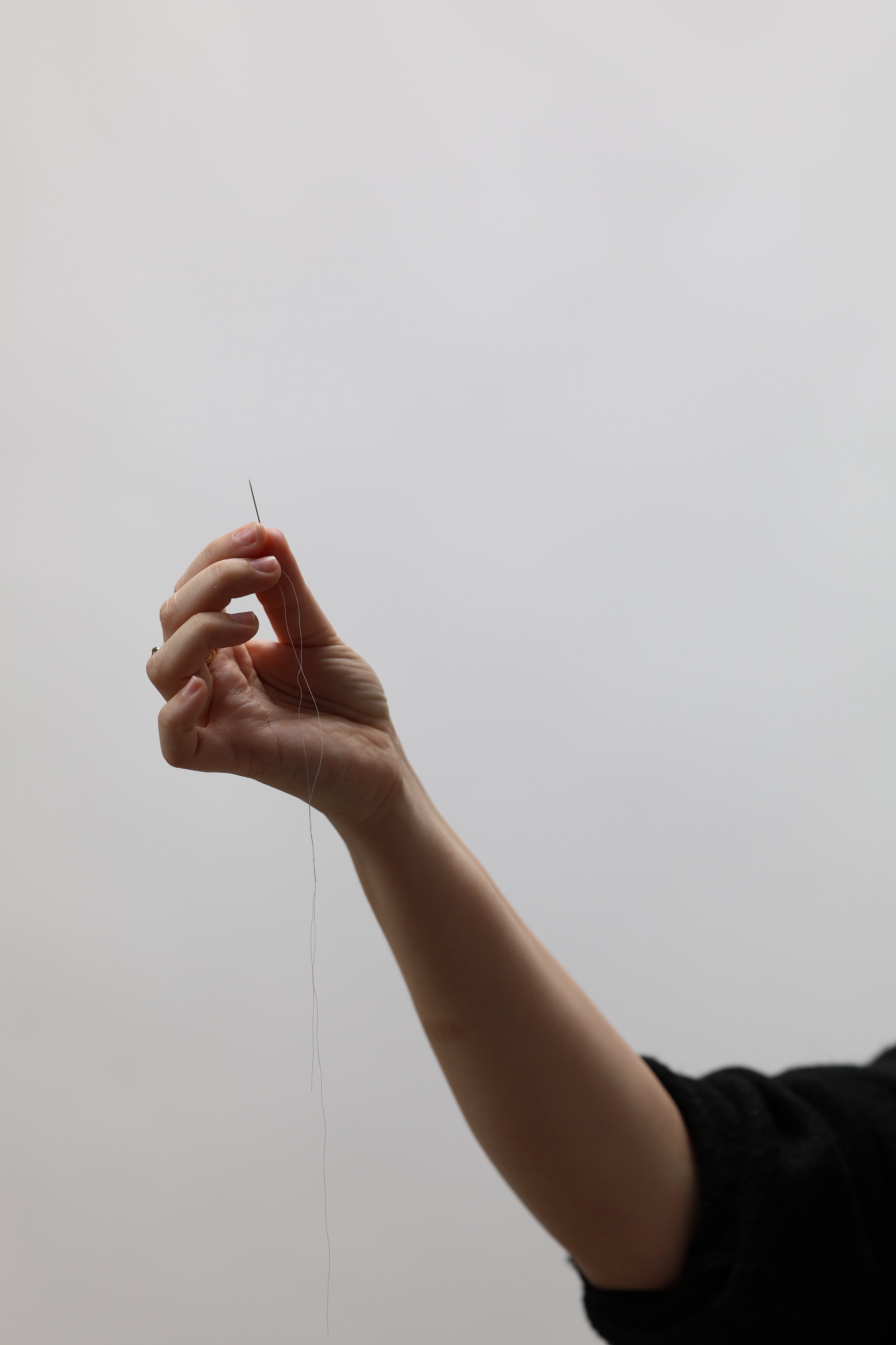 Main tenant une aiguille à coudre avec du fil suspendu.