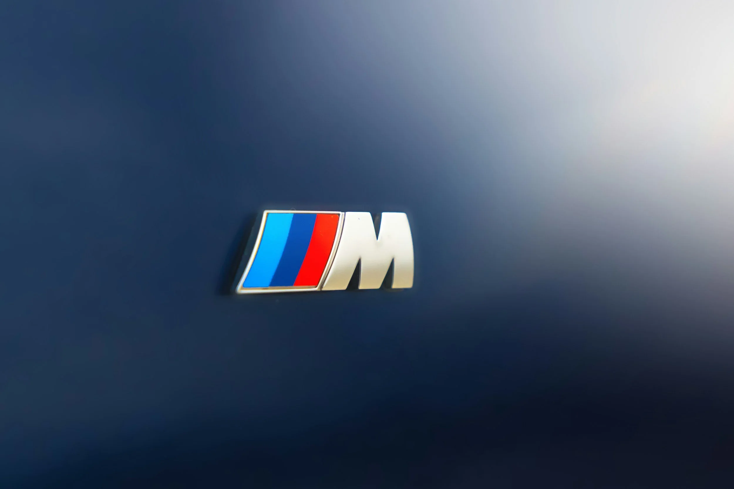 Close-up of a car emblem with the BMW M logo on a dark blue vehicle exterior.