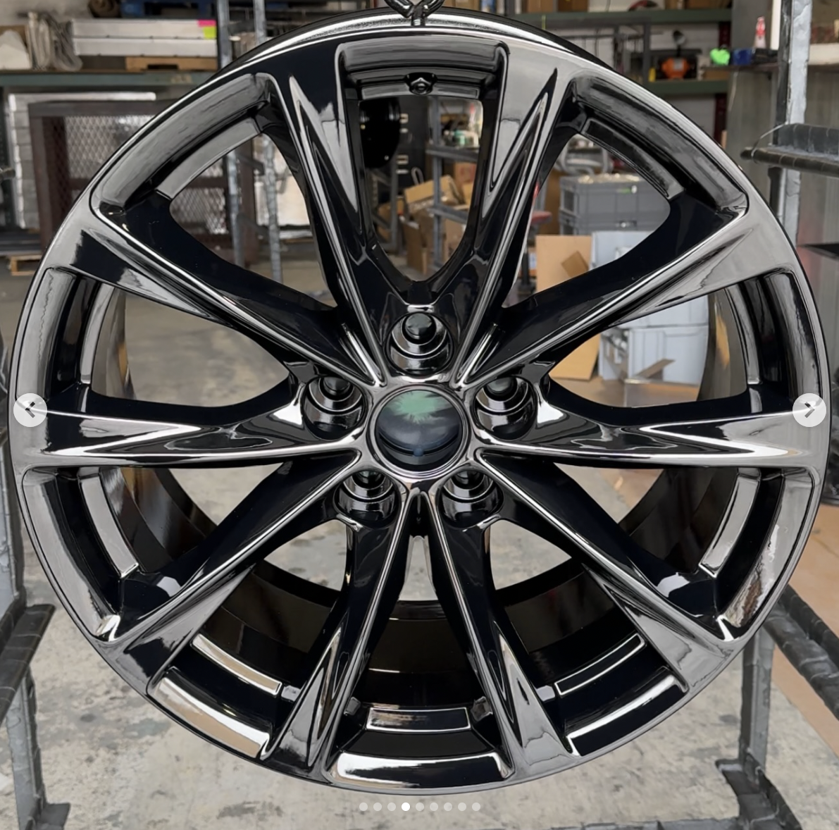A shiny black and silver alloy car wheel with intricate spoke design, mounted on a shelf in a workshop or garage.