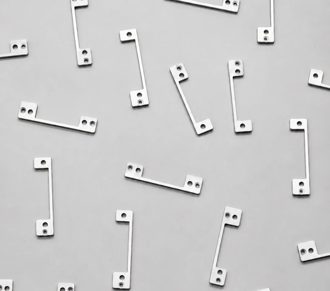 Scattered small white metal brackets with two holes each on a plain gray background.