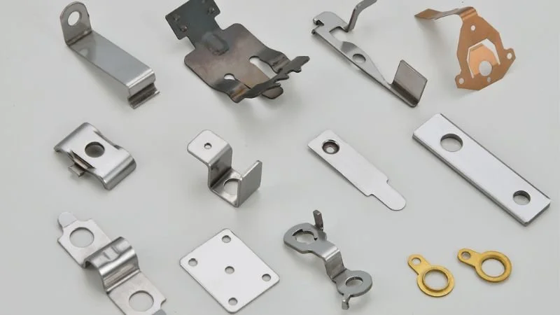 Various small metal and brass hardware clips, brackets, and washers on a white surface.