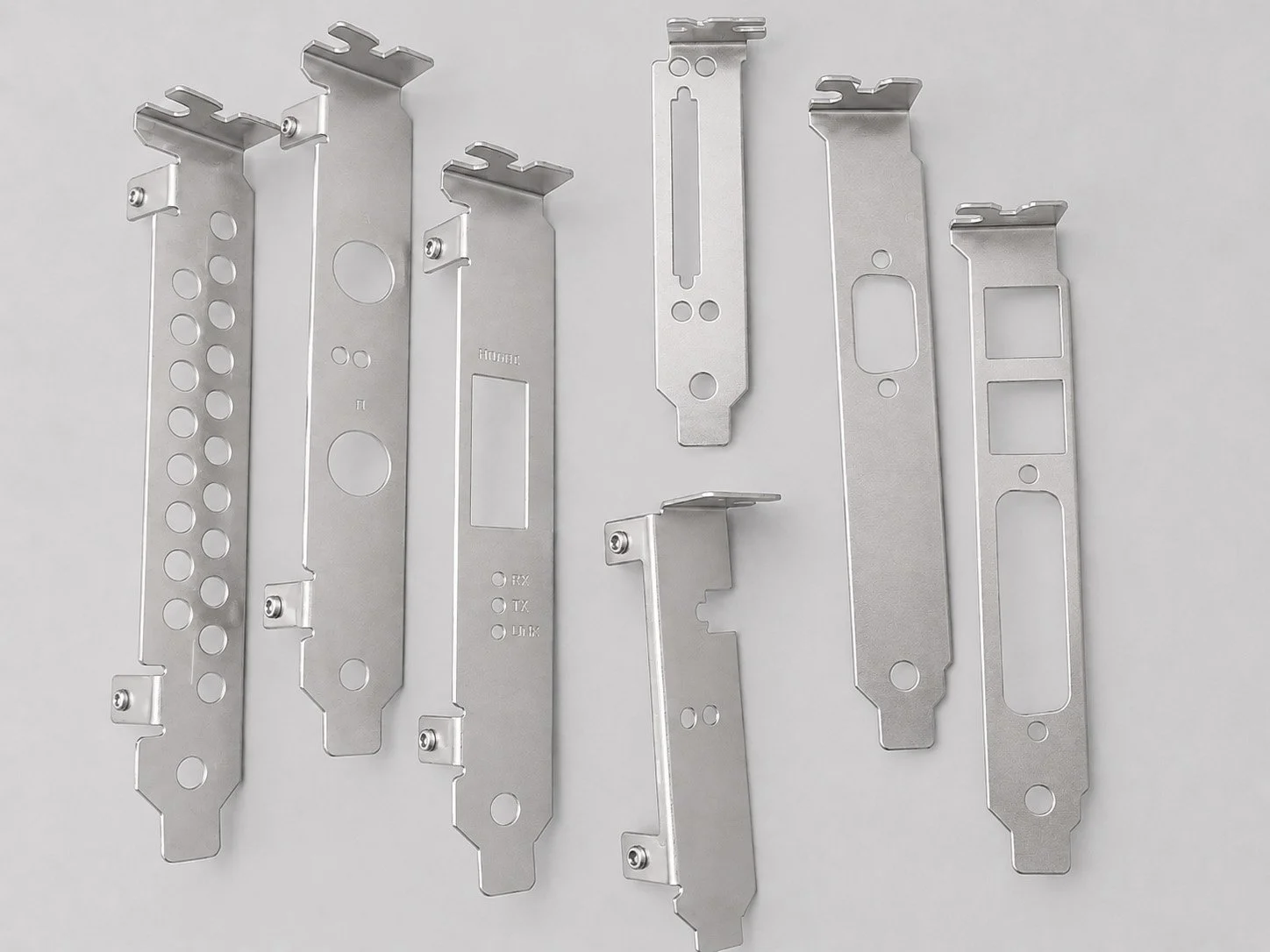 Seven metal mounting brackets with various cutouts and holes, arranged on a light gray background.