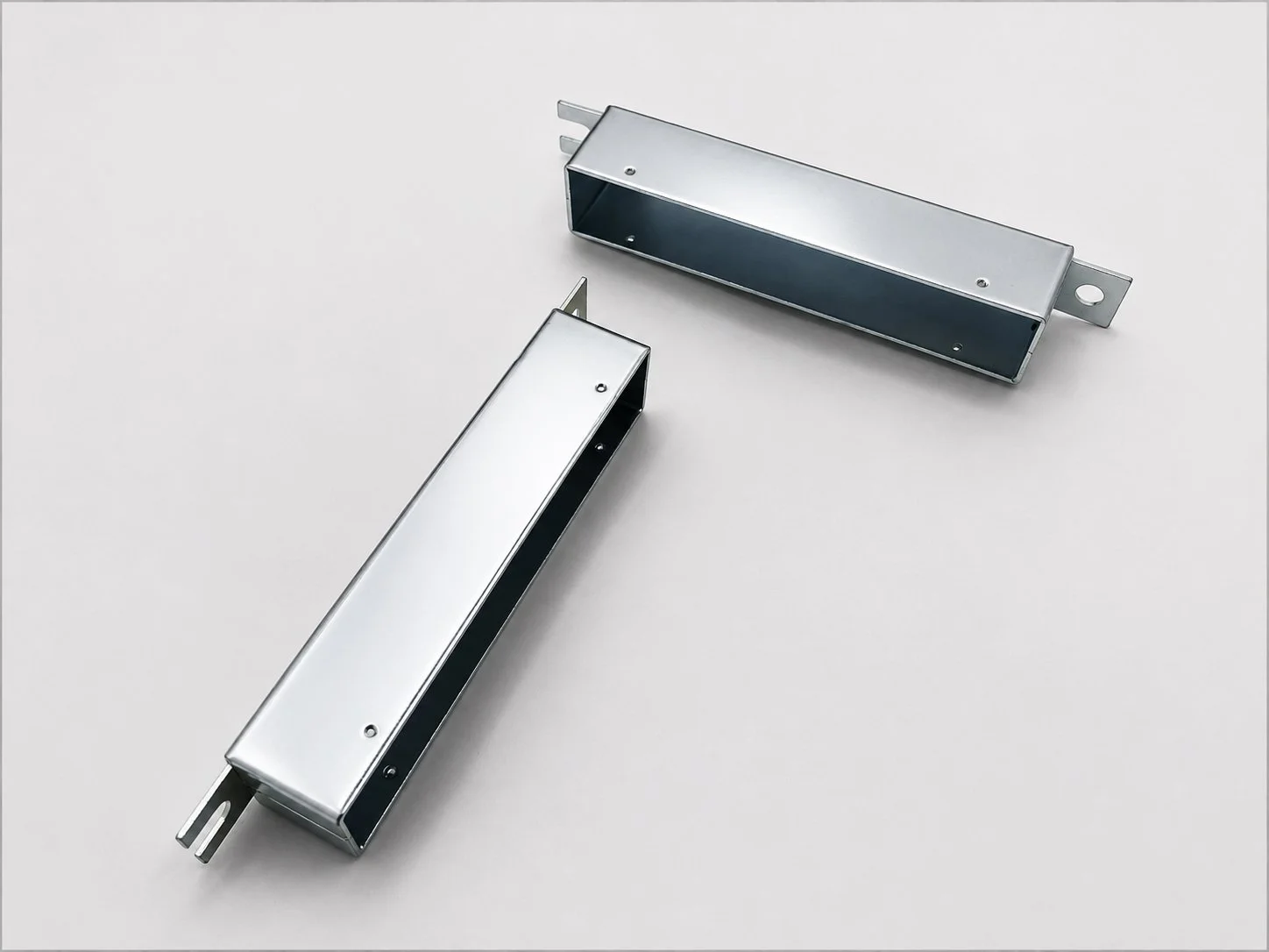 Two metal electrical components on a white surface, one rectangular and open at the top, the other longer and closed.