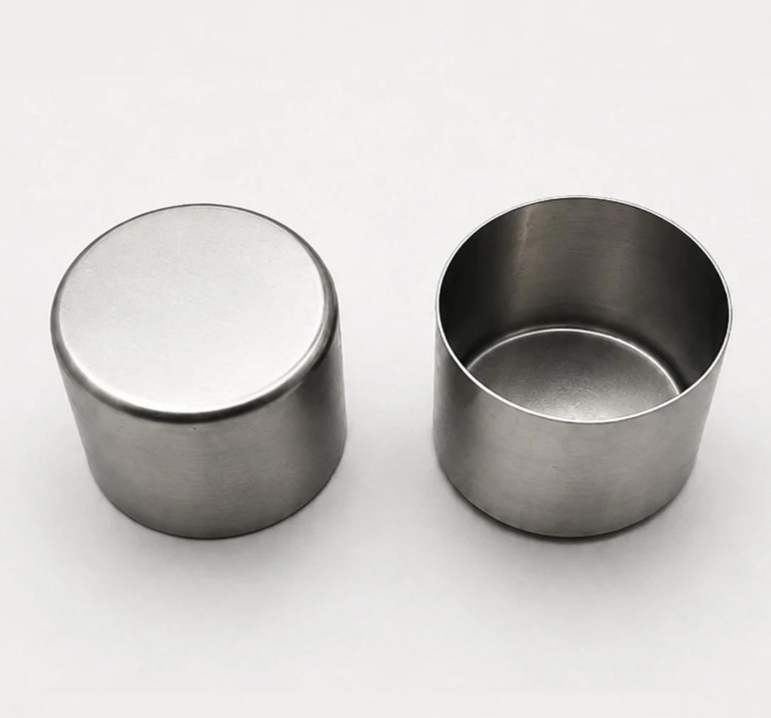 Two silver metal cylindrical containers, one with a lid, placed on a white surface.