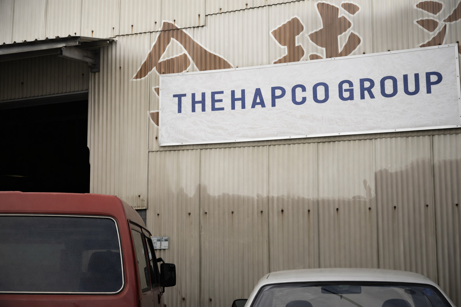 Sign reading 'THEHAPCO GROUP' mounted on a metal building with trucks parked below.
