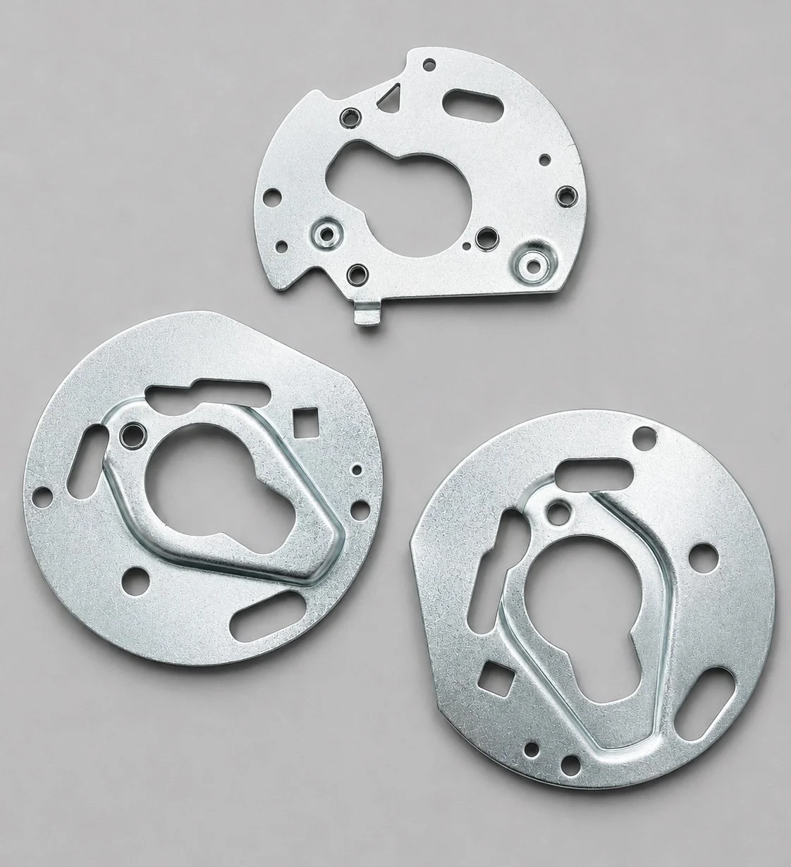 Three metal mechanical parts with multiple holes and cutouts arranged on a gray background.