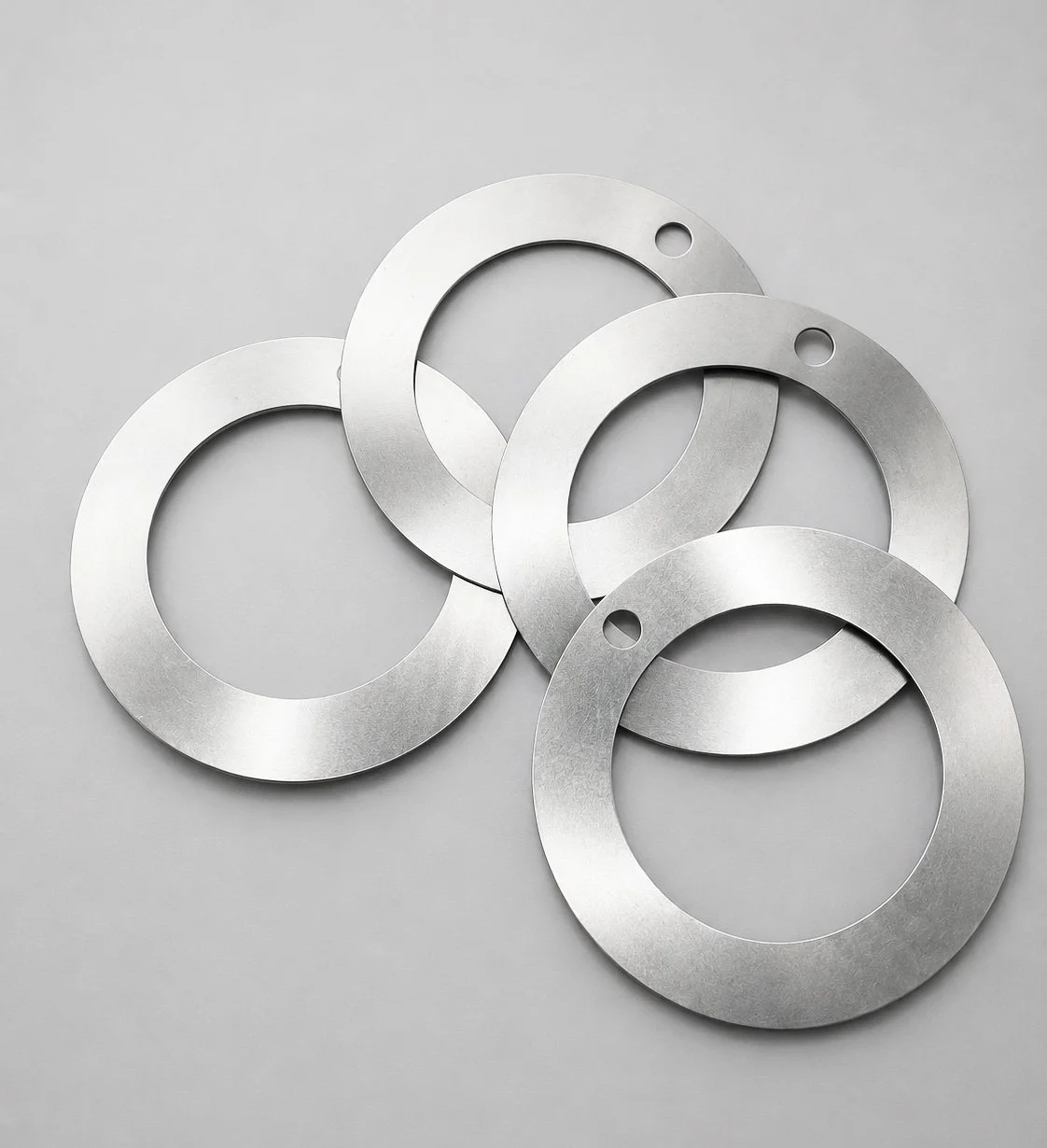 Five metal washers with holes, overlapping on a plain gray surface.