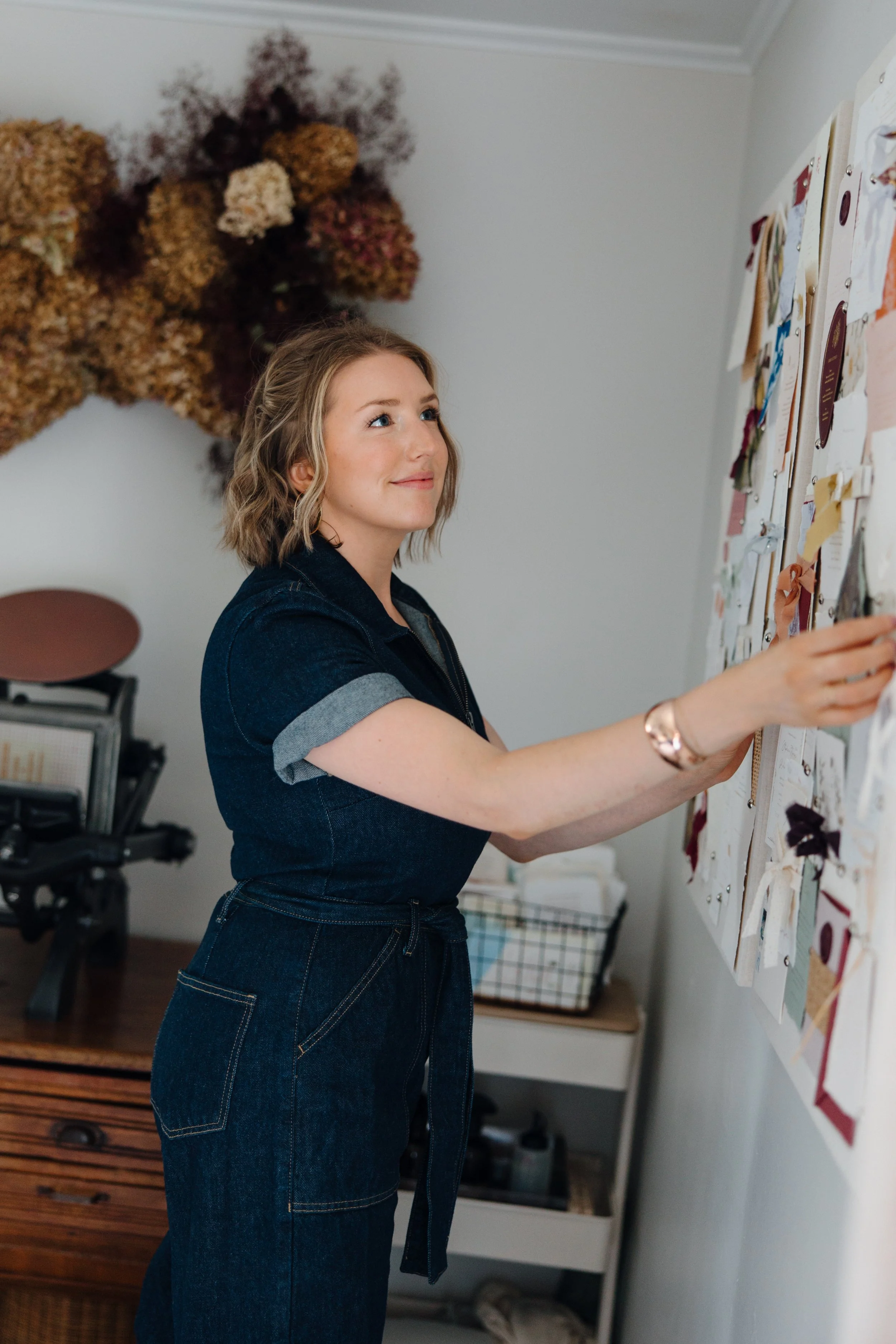 A woman is standing in front of a large display board covered with various paper notes, fabric swatches, and samples, arranging or examining them.