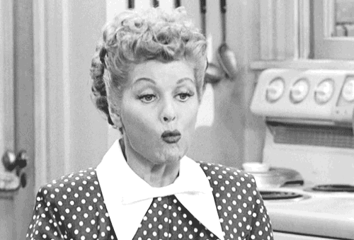 A woman with curly hair wearing a polka-dot dress and white collar, standing in a kitchen.