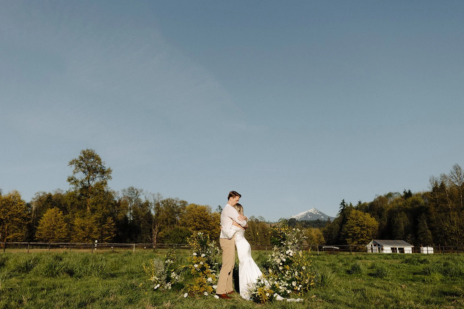 Bride and Groom hugging in a sunny field at Bannan House Farm with lush grass and yellow floral accents