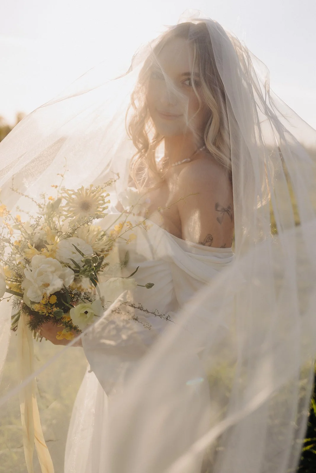 Bride with a veil holding a summer floral bouquet with yellow and white flowers with greenery