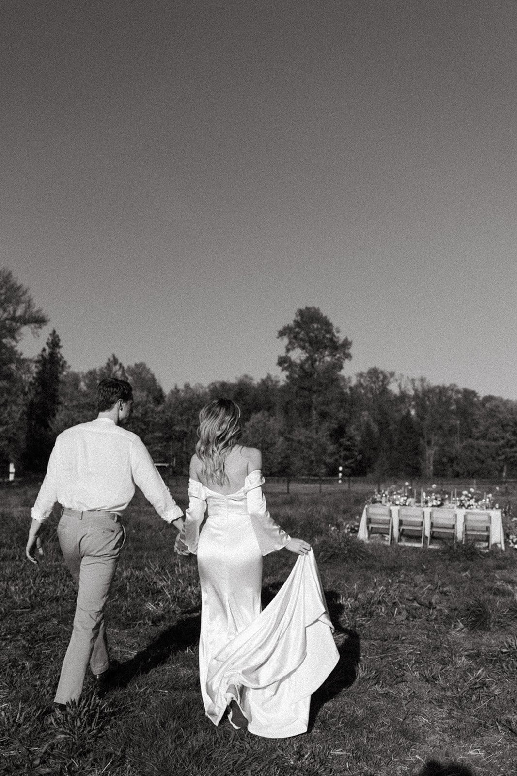 Bride and groom holding hands in a field walking towards their reception