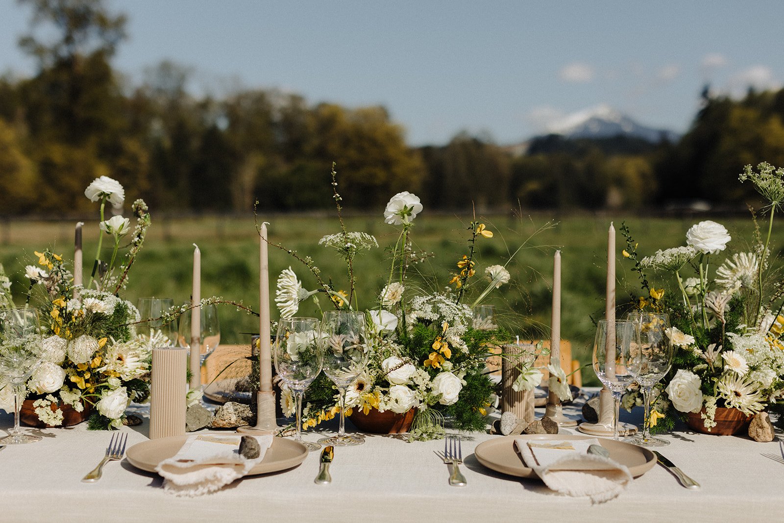 Table setting with summer florals with yellow and white flowers and greenery in a grass field