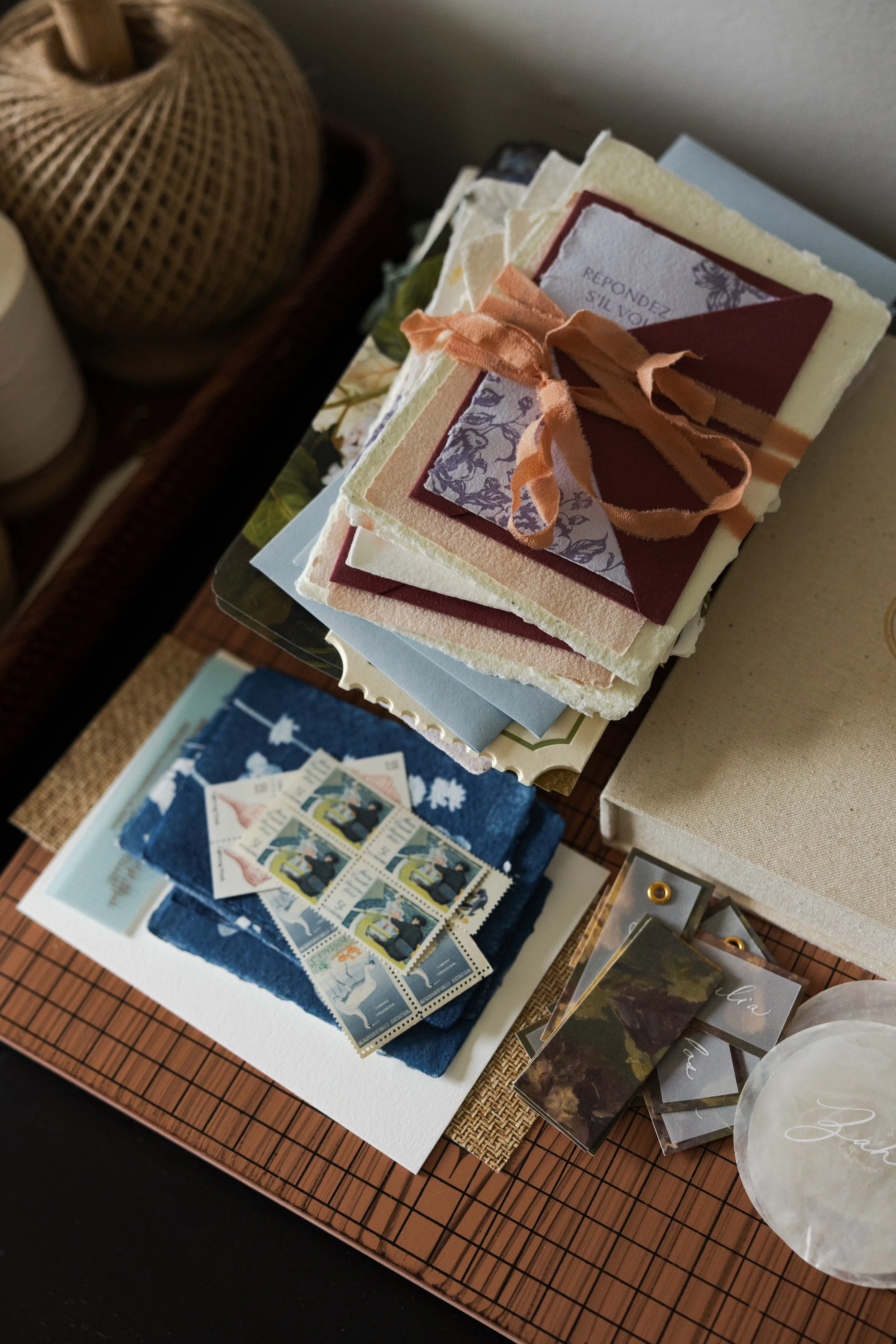 Stack of assorted handmade paper and greeting cards on a table, with stamps and decorative items nearby.