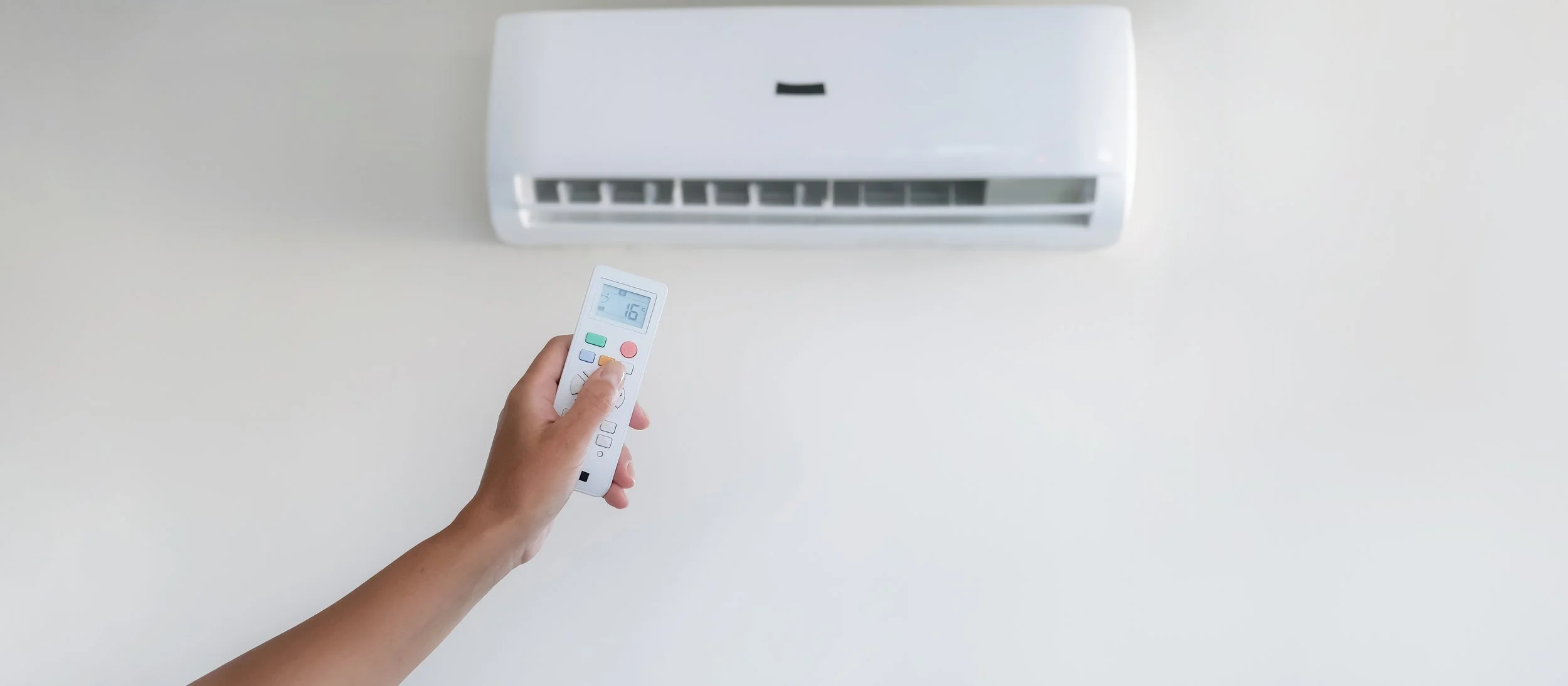 The image shows an air conditioning unit in the background, with a hand holding a remote in the foreground