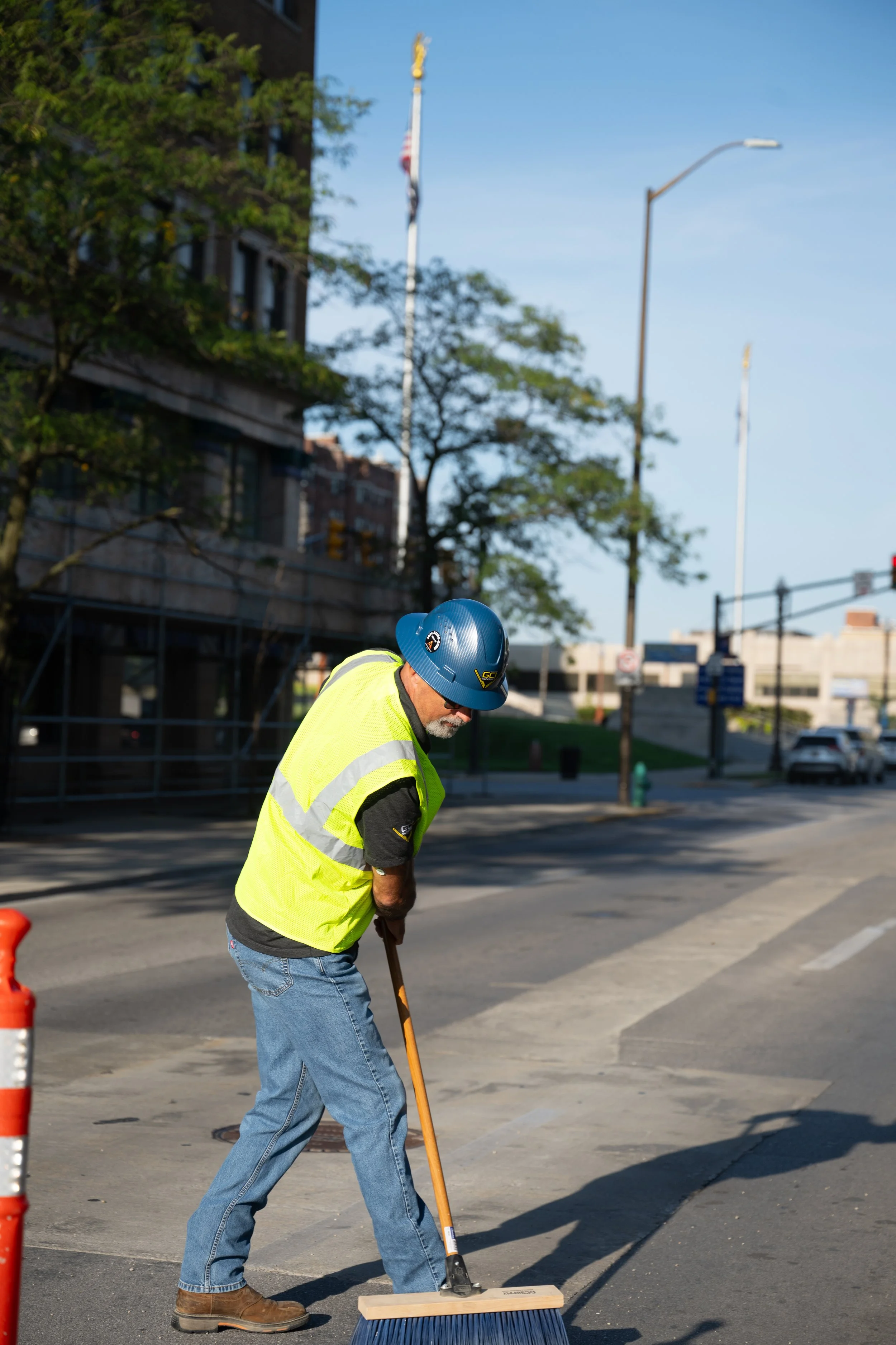 A GCI employee in a vest and construction hat sweeping a street