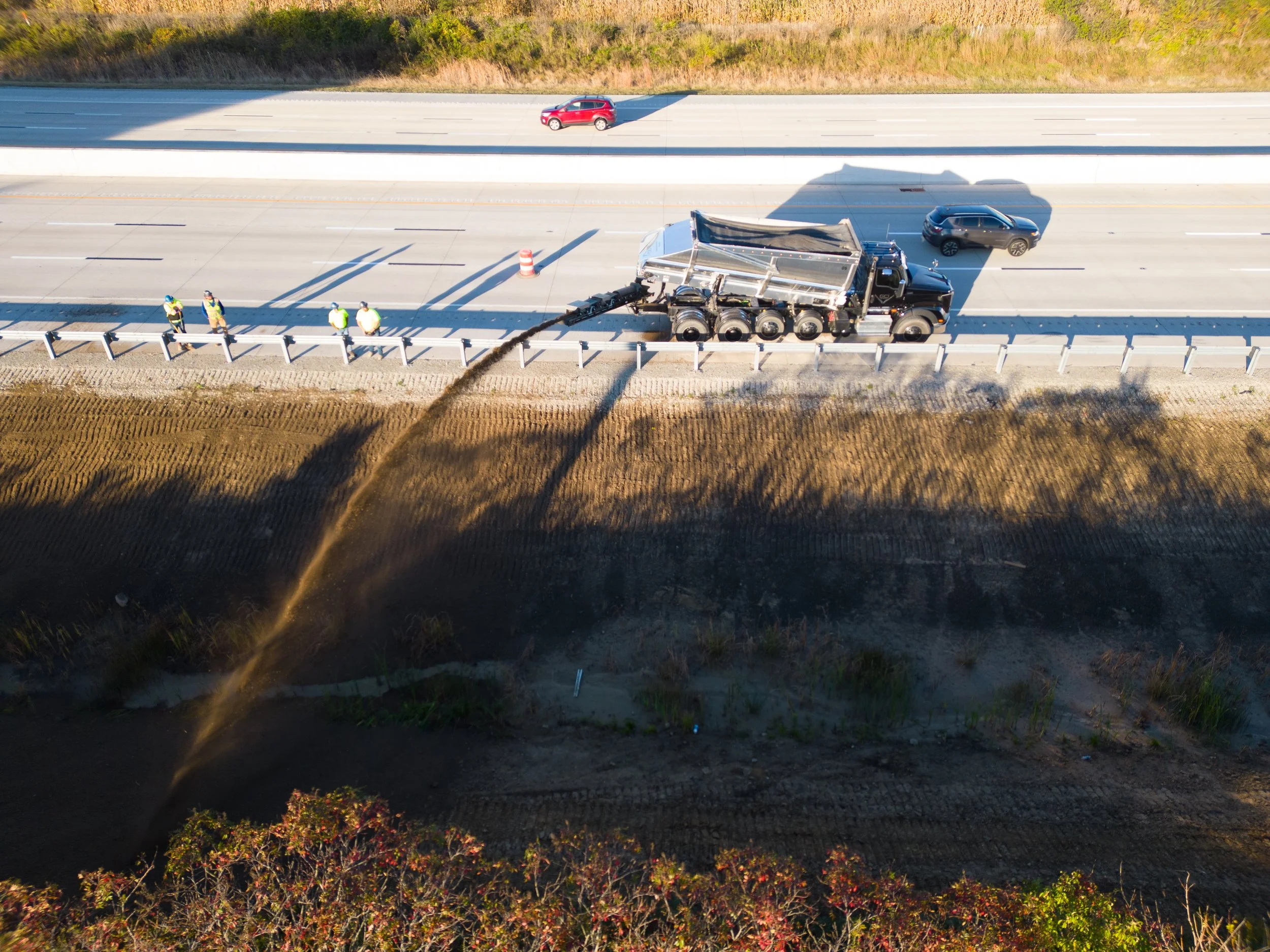 A truck slinging materials into a ditch on the side of the road