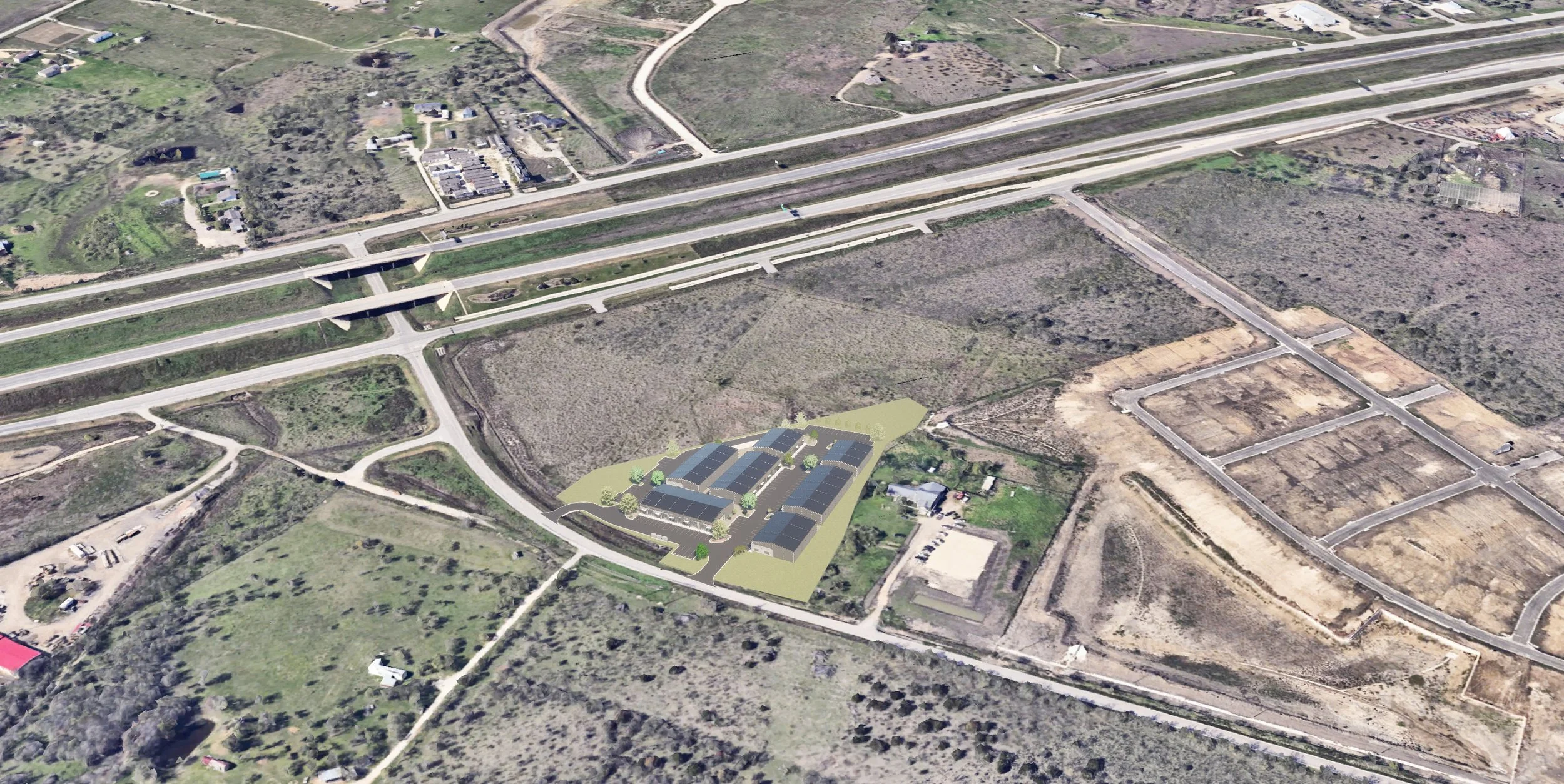 Aerial view of a construction site with newly built and planned buildings, roads, and open land surrounded by natural terrain and existing infrastructure.