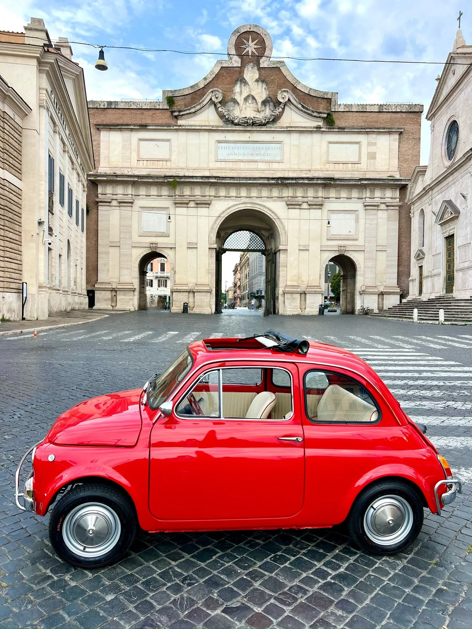 Auto rossa vecchia davanti a un arco storico in Italia