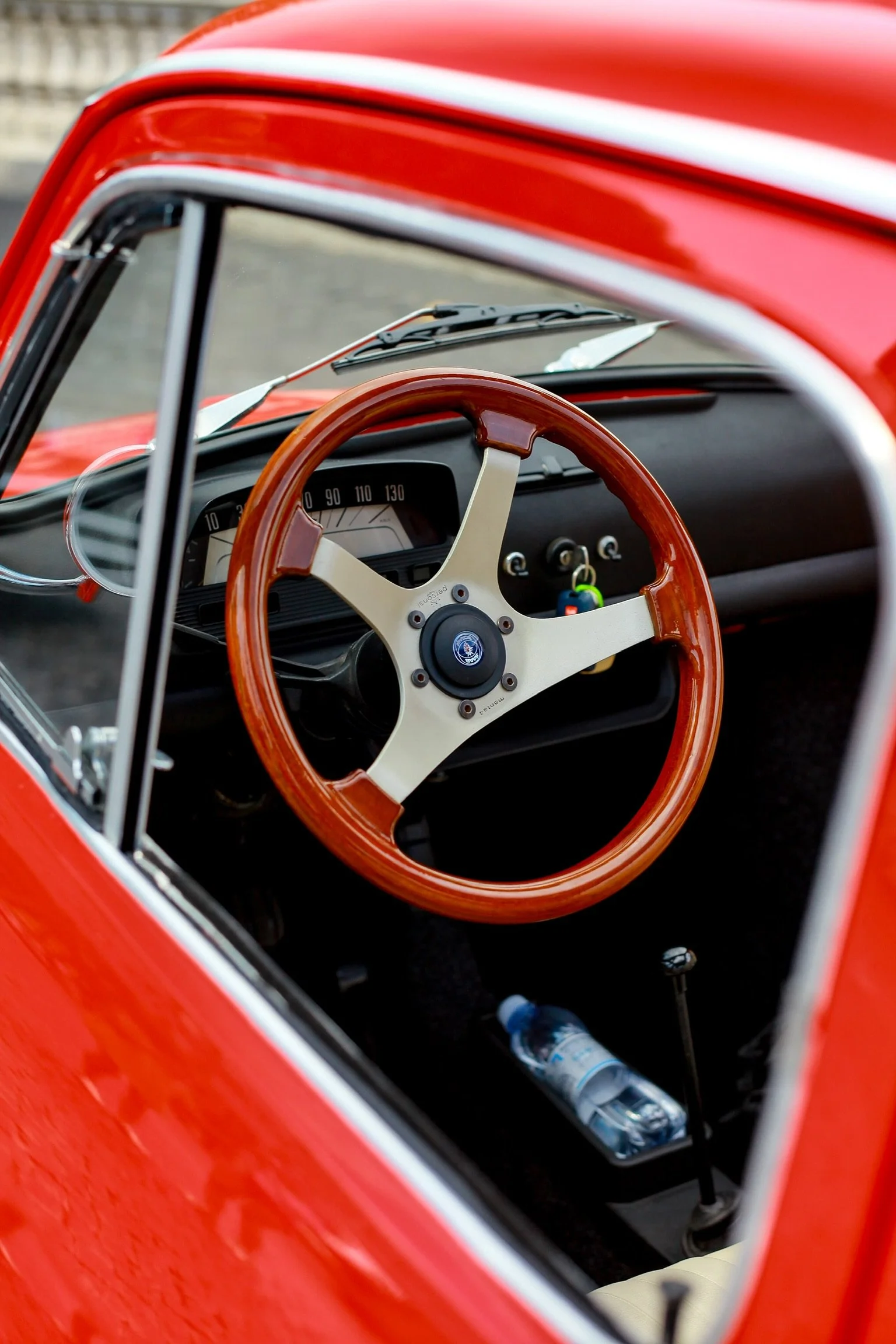 Interno di un'auto d'epoca rossa, con volante in legno, display analogico, e chiavi nel quadro strumenti.