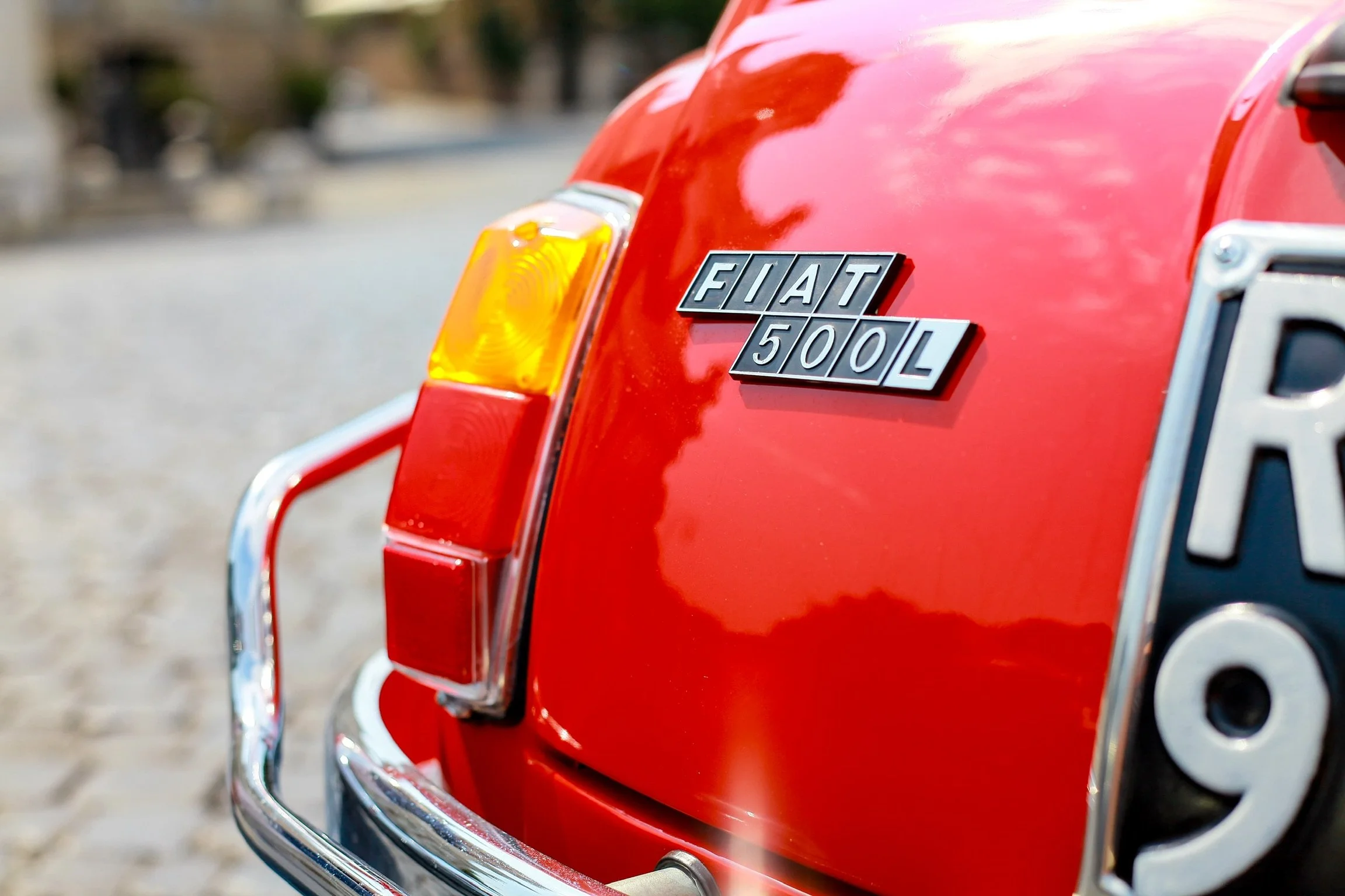 Dettaglio posteriore di una Fiat 500L rossa, con badge e parte di uno spigolo di una targa visibile.