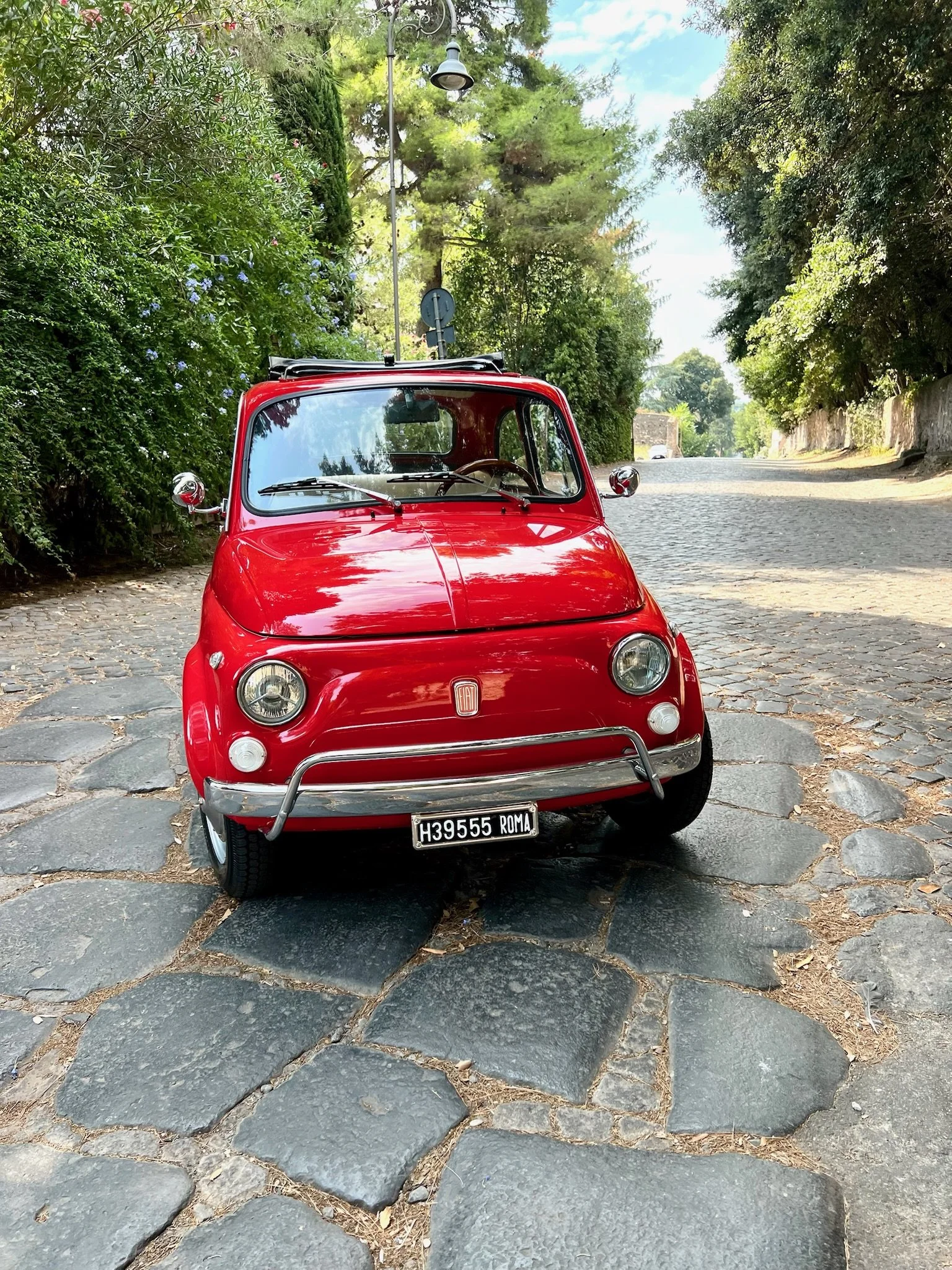 Auto d'epoca rossa parcheggiata su una strada acciottolata circondata da alberi verdi.