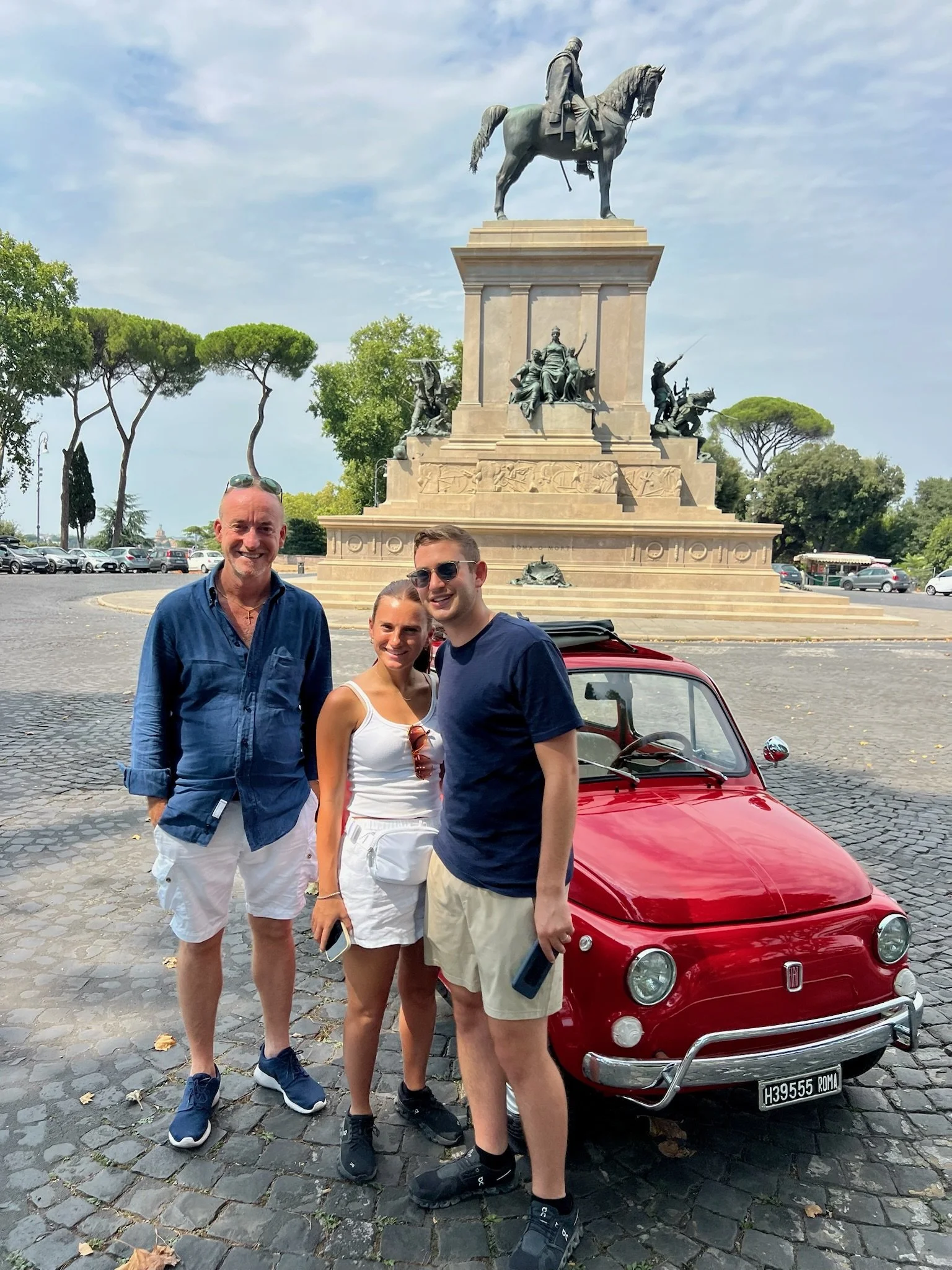 Tre persone sono davanti a un'auto rossa e una statua di un generale in sella a cavallo a Roma.