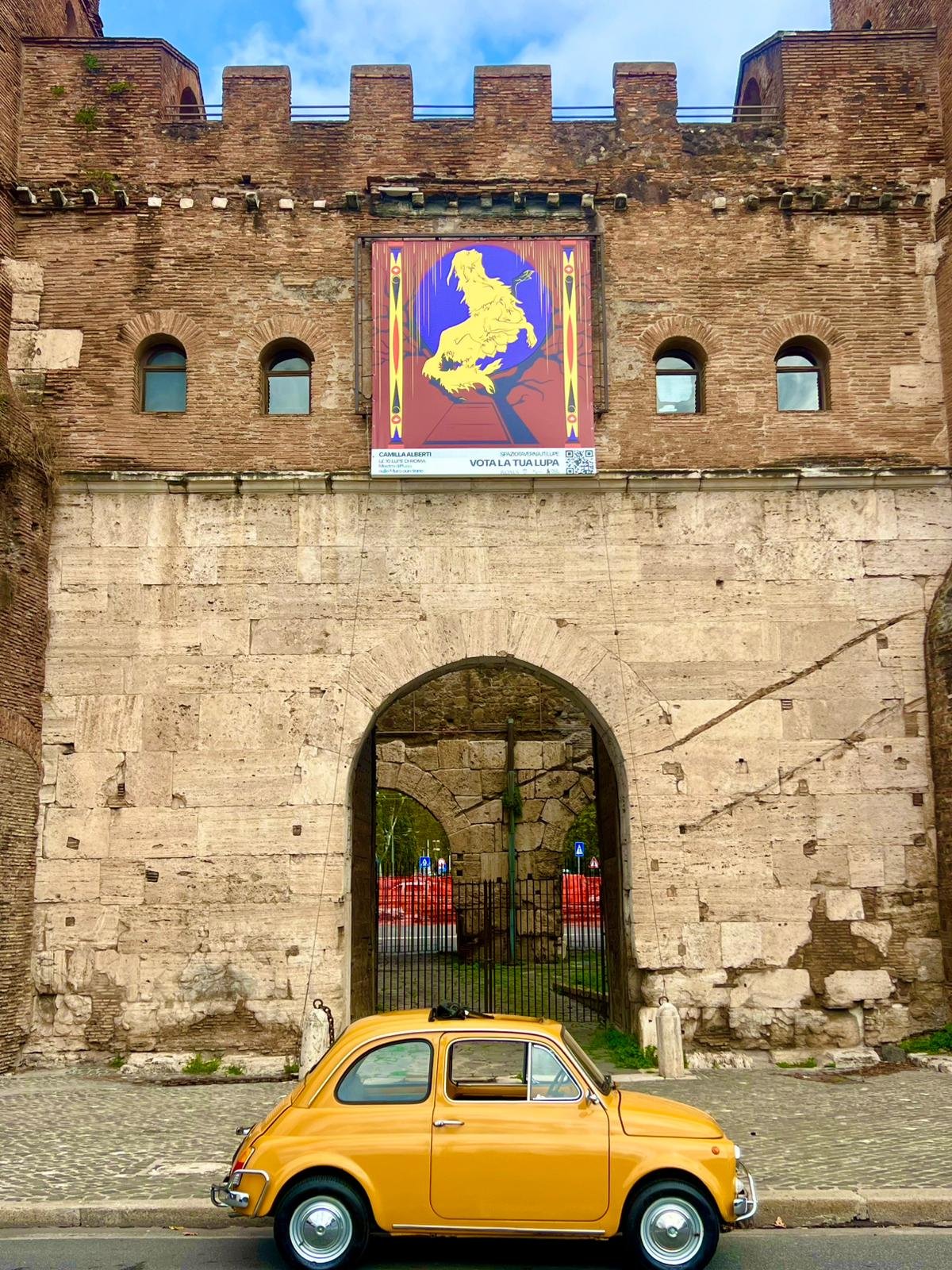 Un edificio antico di mattoni con un arco in pietra che dà su un cortile, e una macchina d'epoca gialla parcheggiata davanti all'arco.