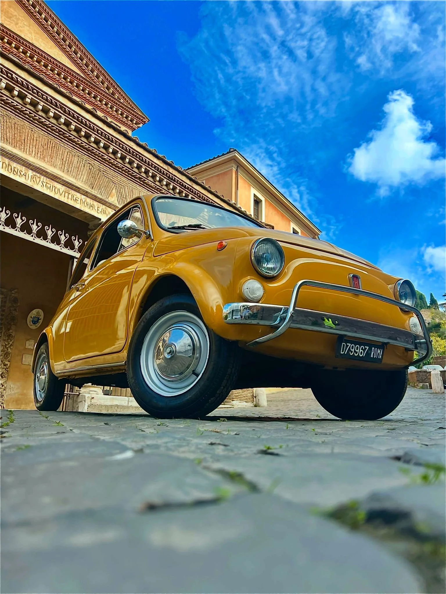 Auto d'epoca gialla parcheggiata davanti a un edificio in un giorno di cielo sereno.