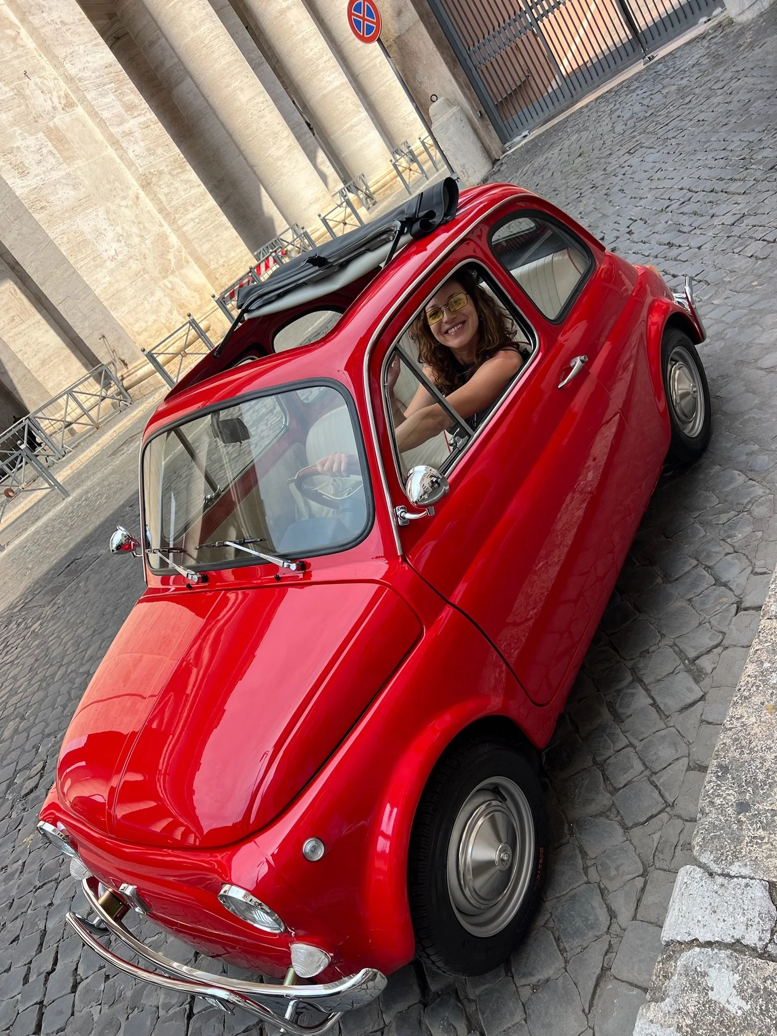 Donna in auto rossa decappottabile d'epoca in via, sorriso e occhiali gialli