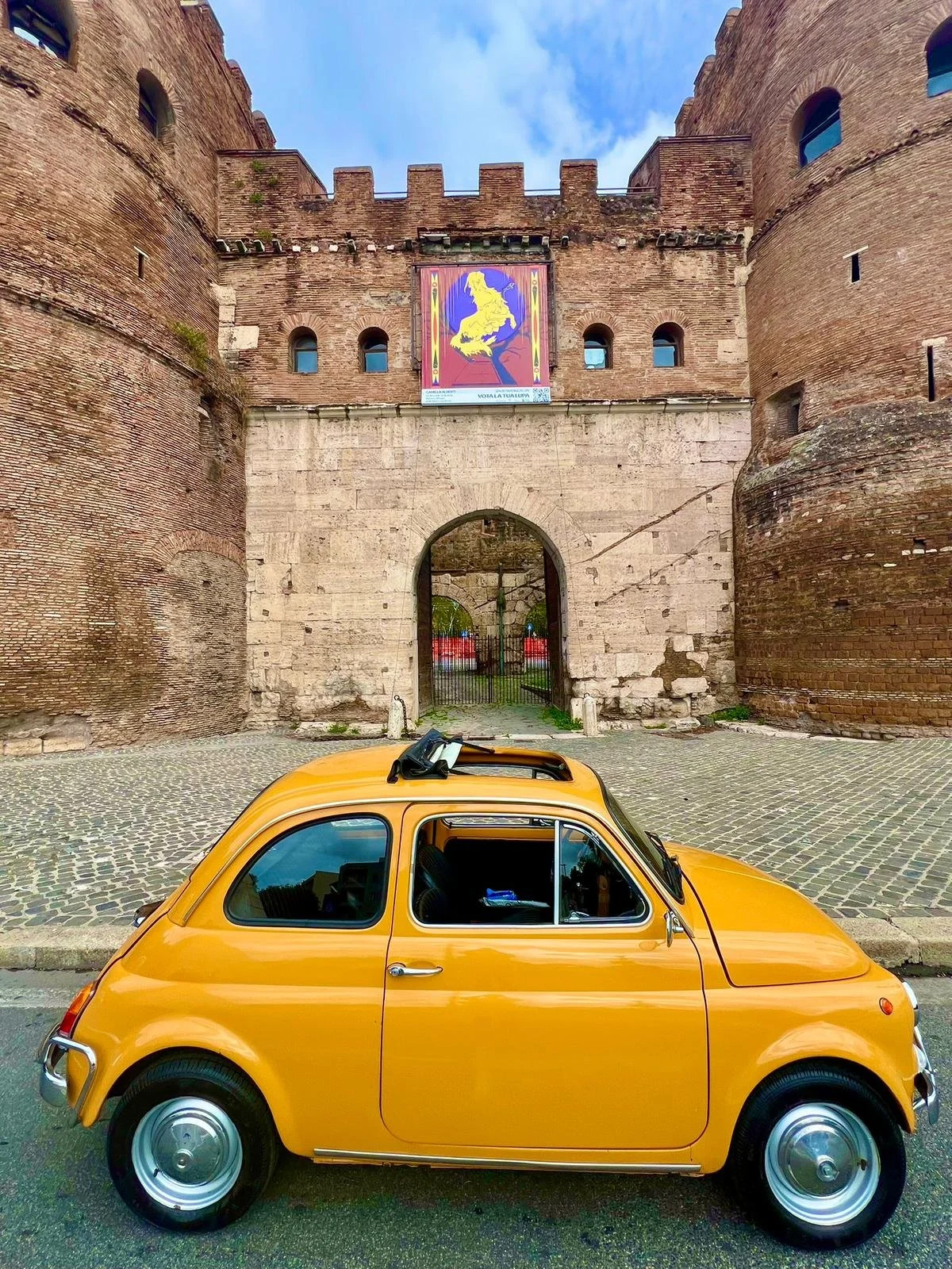 Un'auto di colore giallo parcheggiata davanti a una porta di un castello di mattoni.