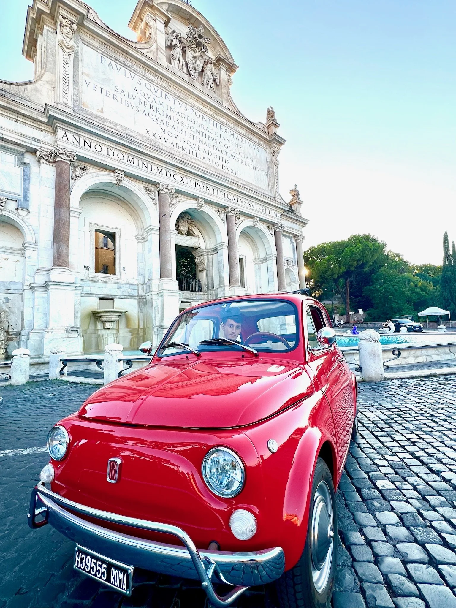 Auto Fiat rossa parcheggiata davanti a un edificio storico in pietra con iscrizioni latine.