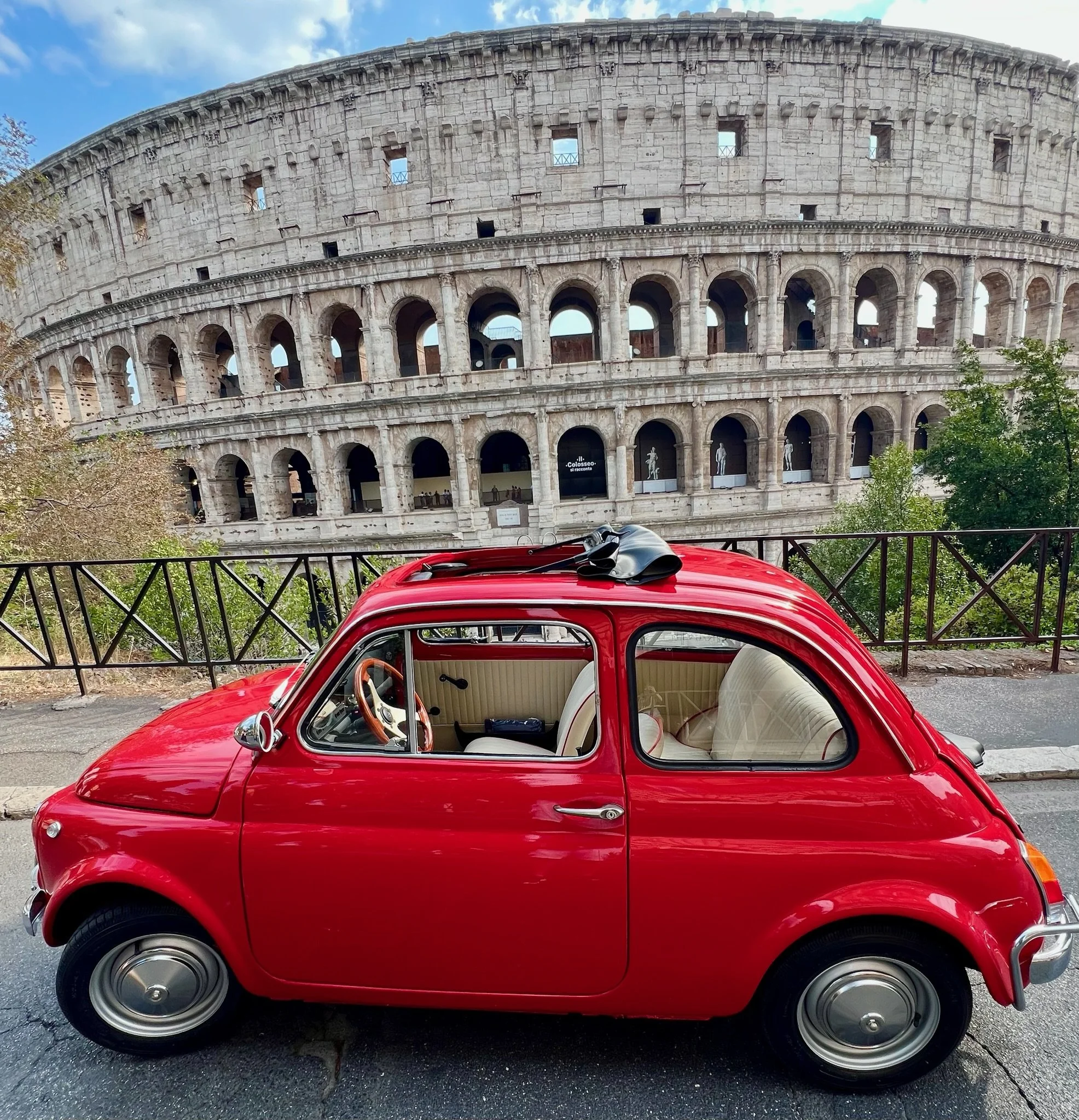 Auto compatta rossa parcheggiata davanti al Colosseo a Roma, Italia.